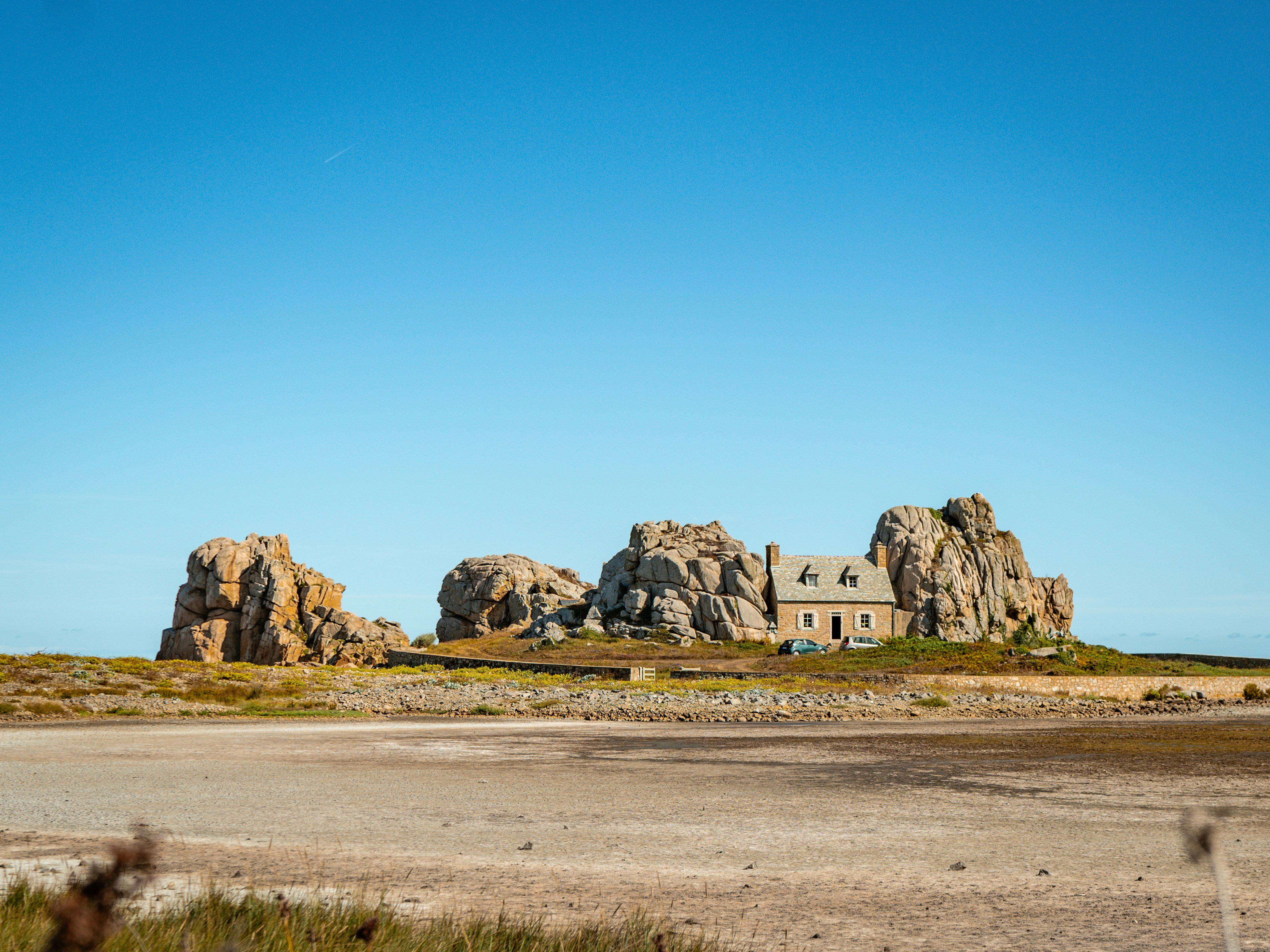 A stone house nestled between large granite boulders on a coastal landscape