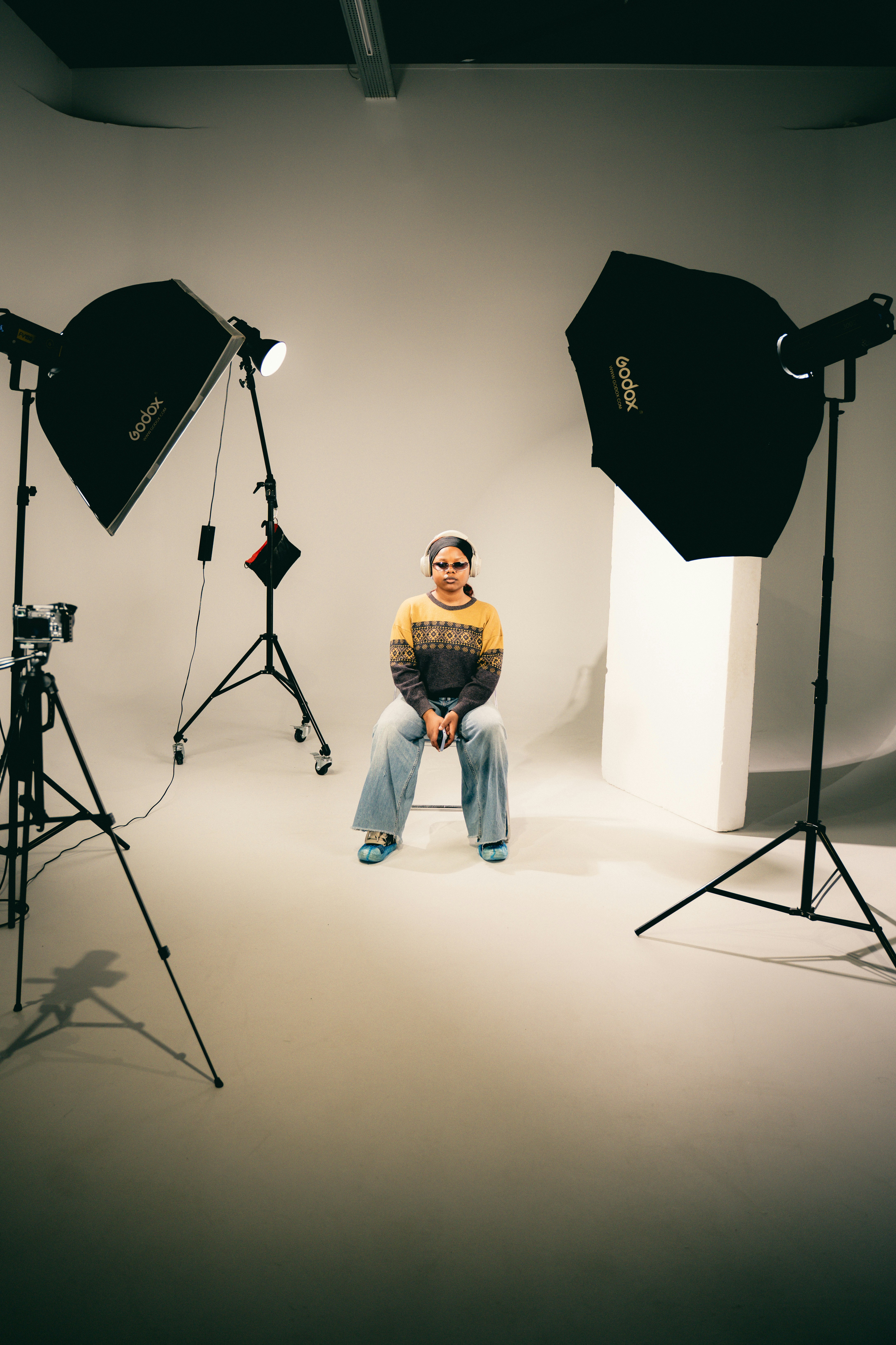 A person in a patterned sweater and jeans sitting in a studio with lighting equipment