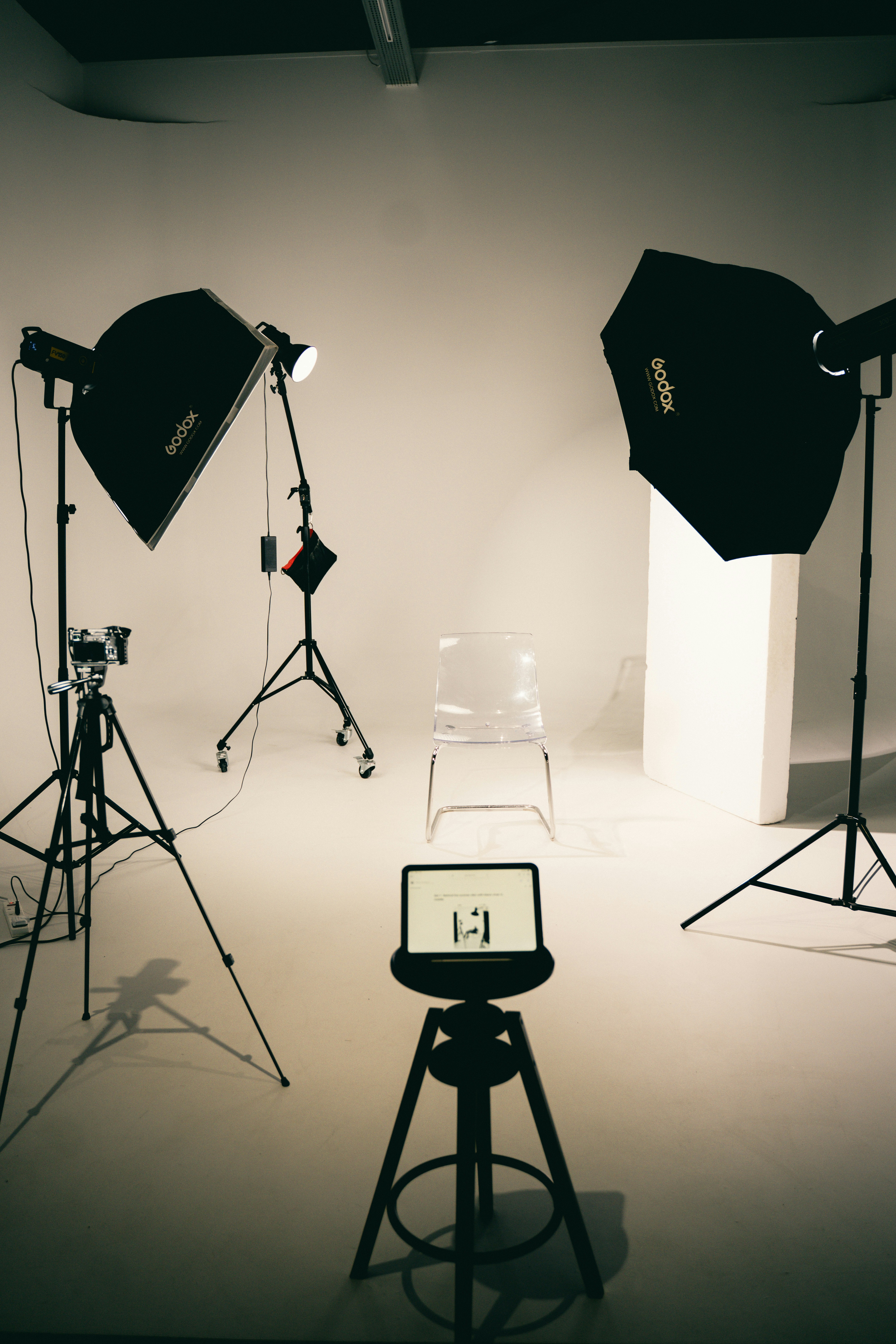 A clear plastic chair in a photography studio with two softbox lights and a camera on a tripod