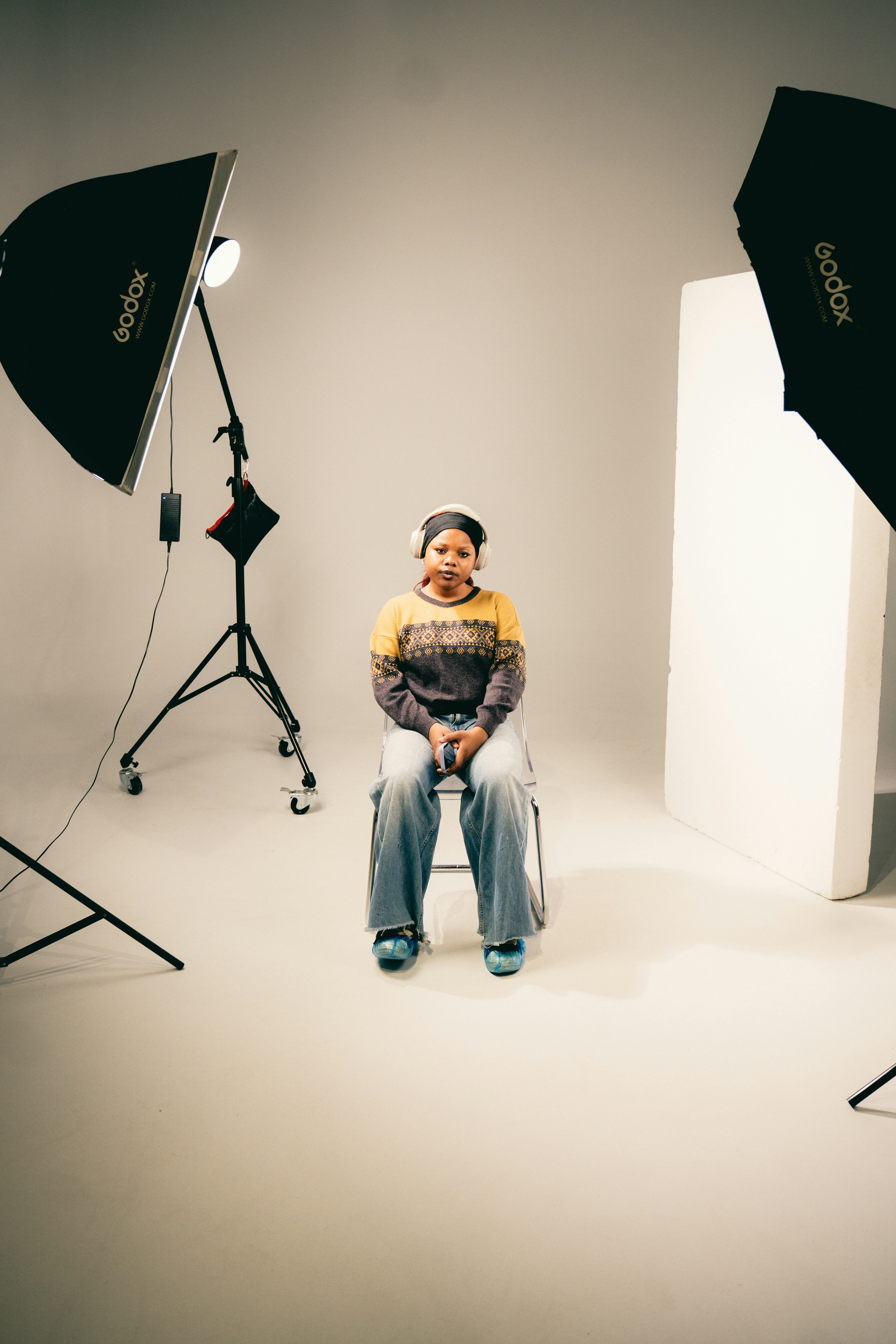 A person wearing headphones and a patterned sweater sitting on a chair in a studio