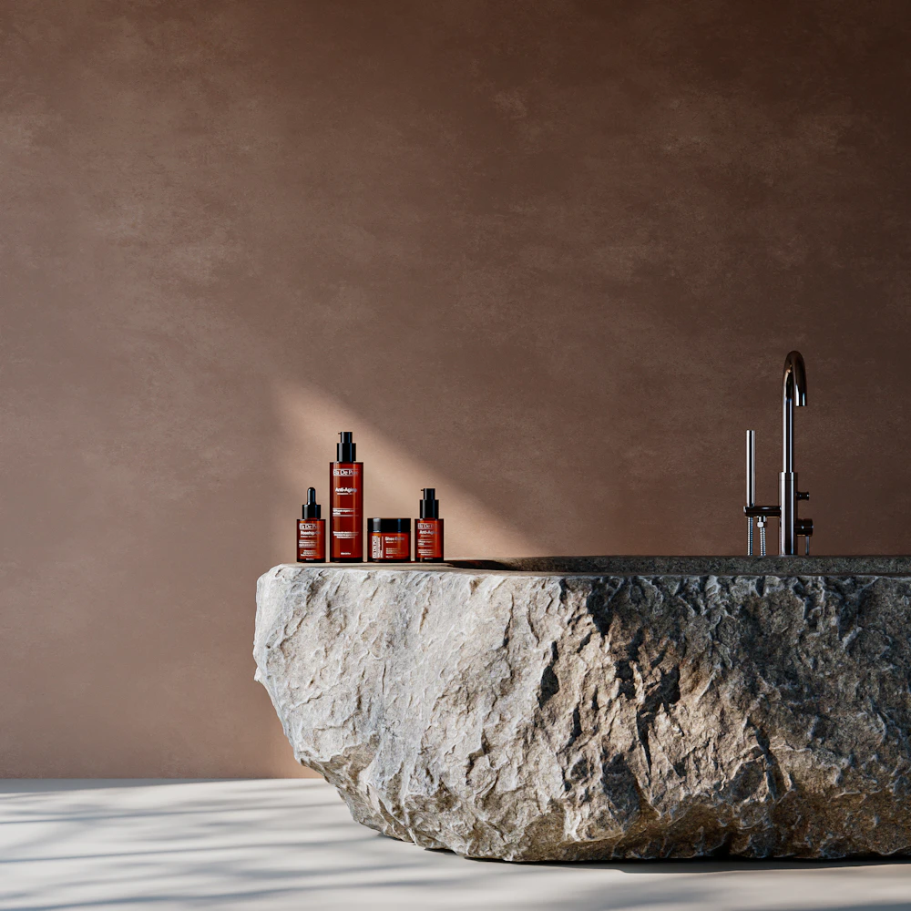 Four amber skincare bottles on a rough stone basin against a warm brown wall