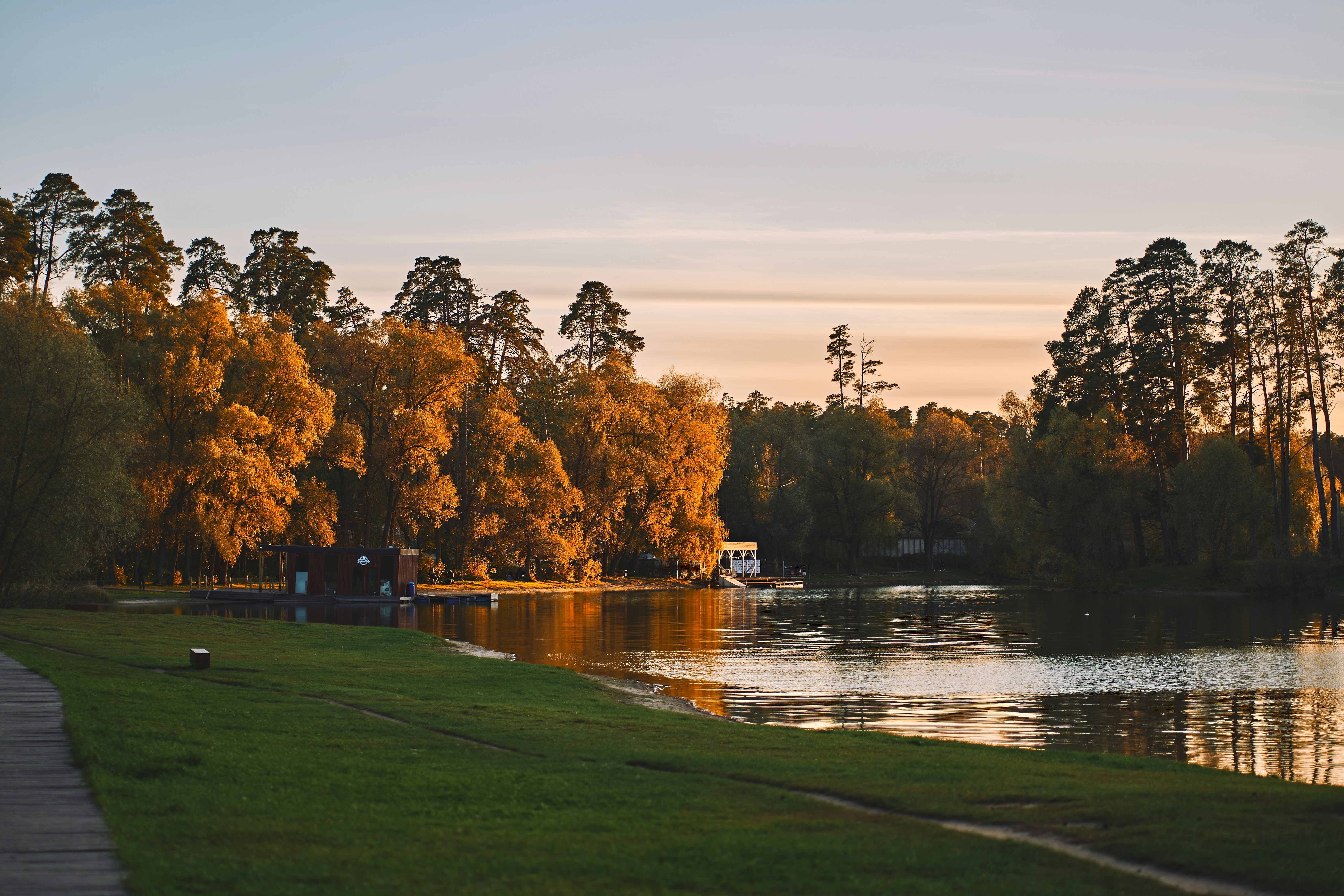 A calm lake reflecting golden autumn trees under a soft light sky