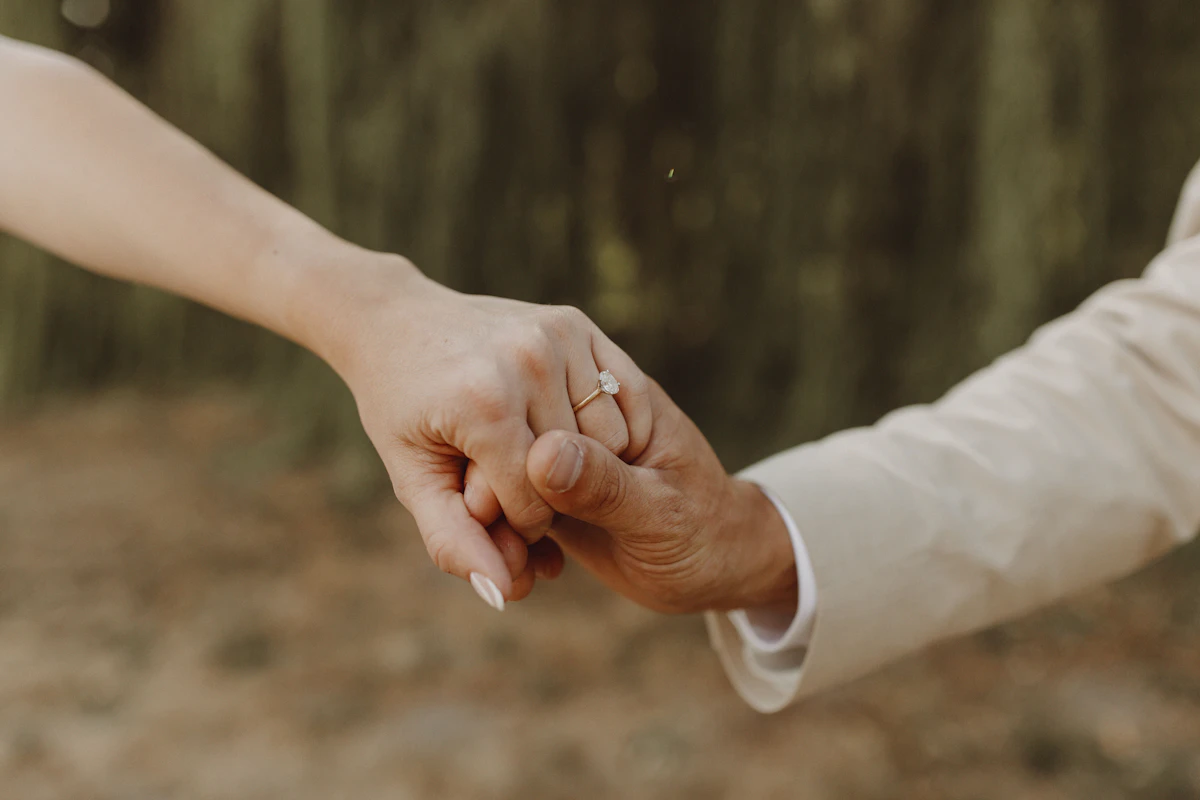 Dua orang bergandengan tangan dengan cincin pertunangan