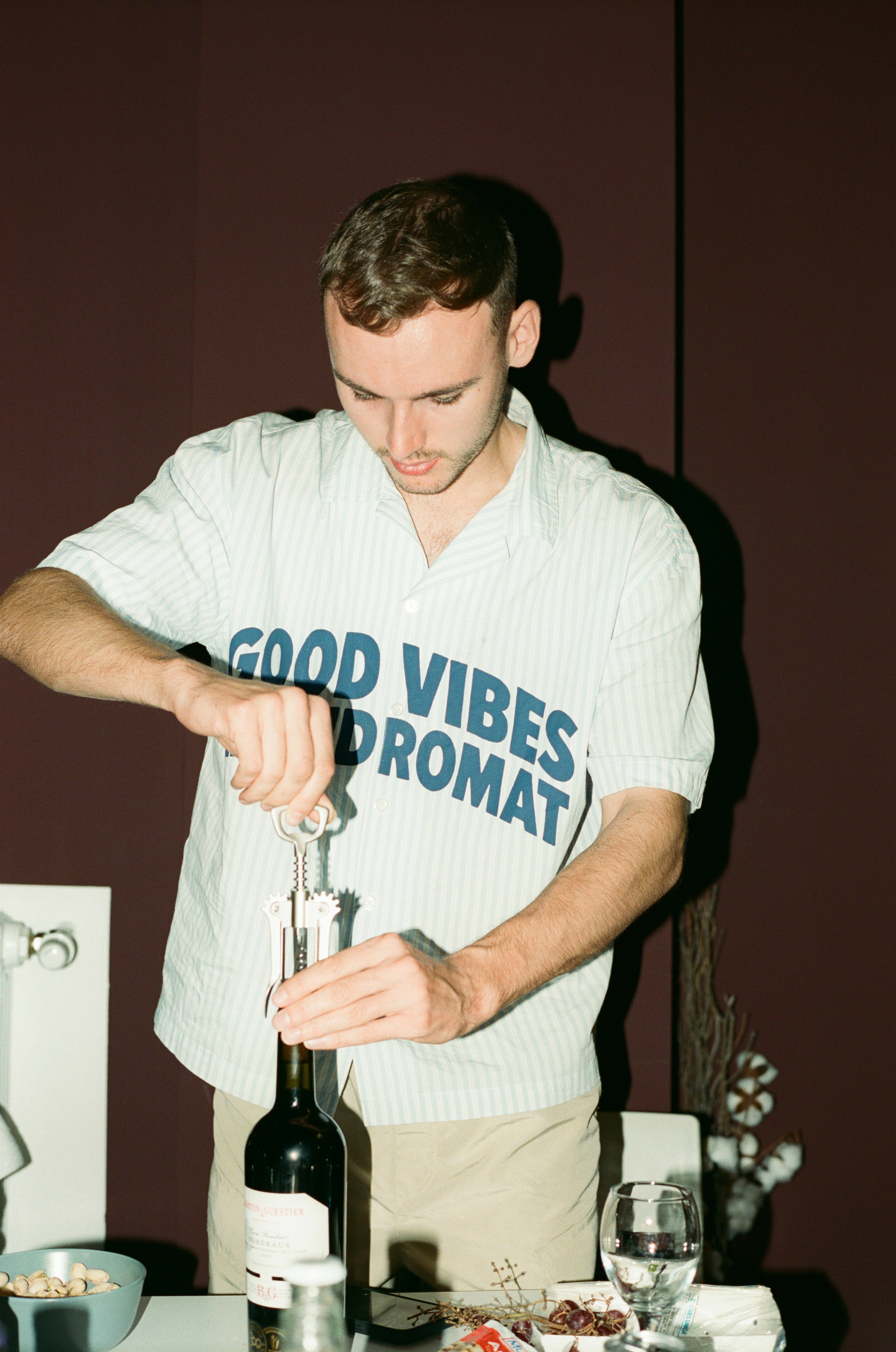 A man in a striped shirt opening a wine bottle with a corkscrew