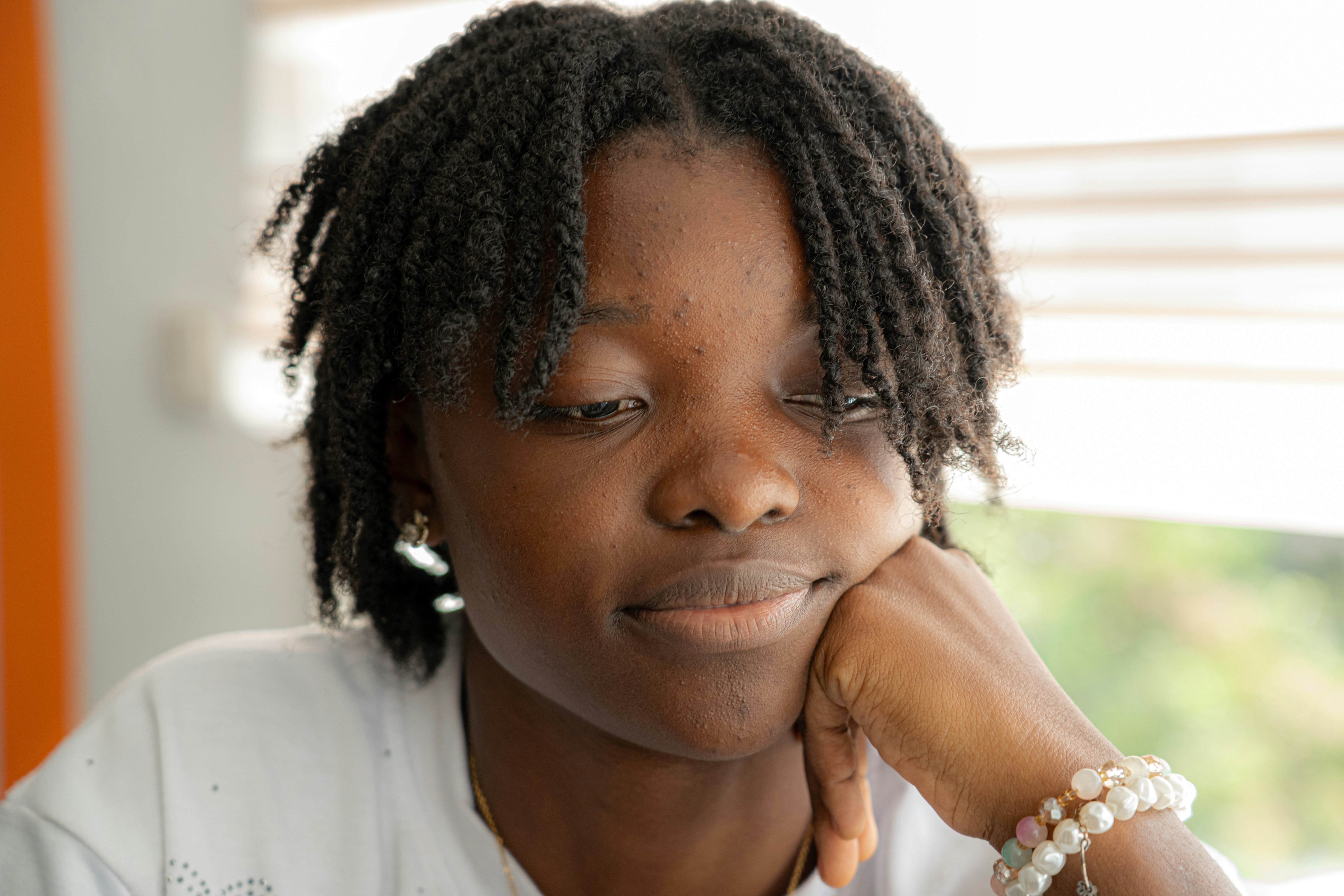 A person with dark braided hair resting their chin on a hand