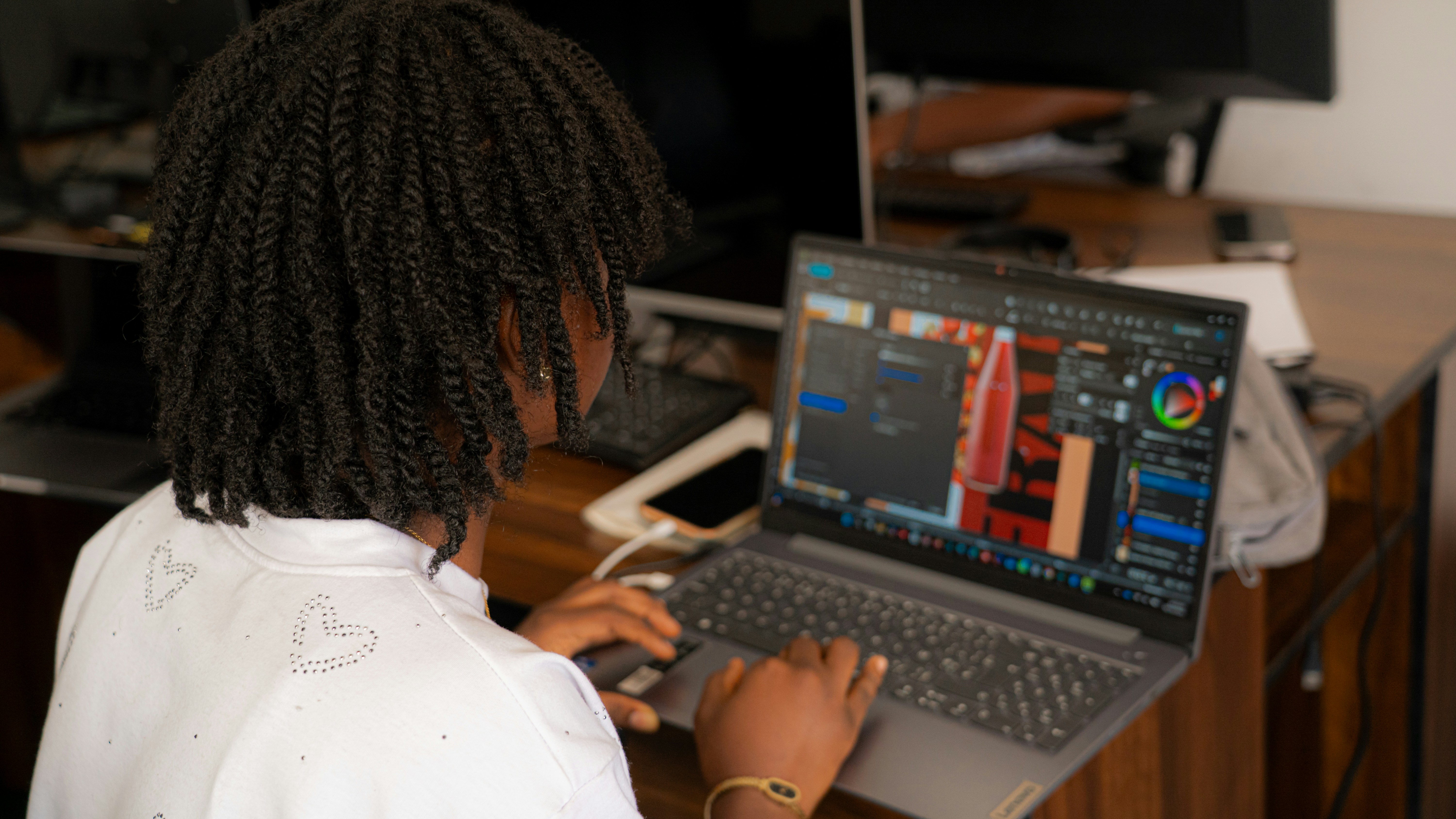 A person with braided hair using a laptop at a wooden desk