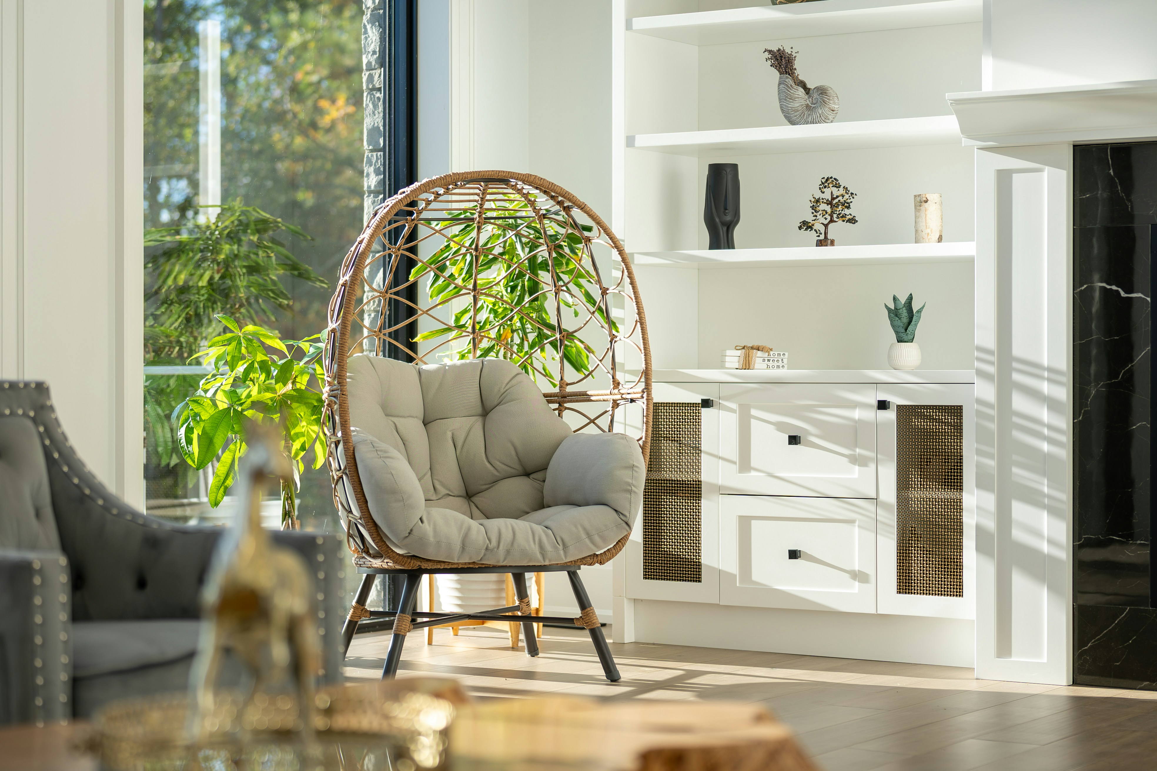 A rattan egg chair with a grey cushion in a sunlit living room