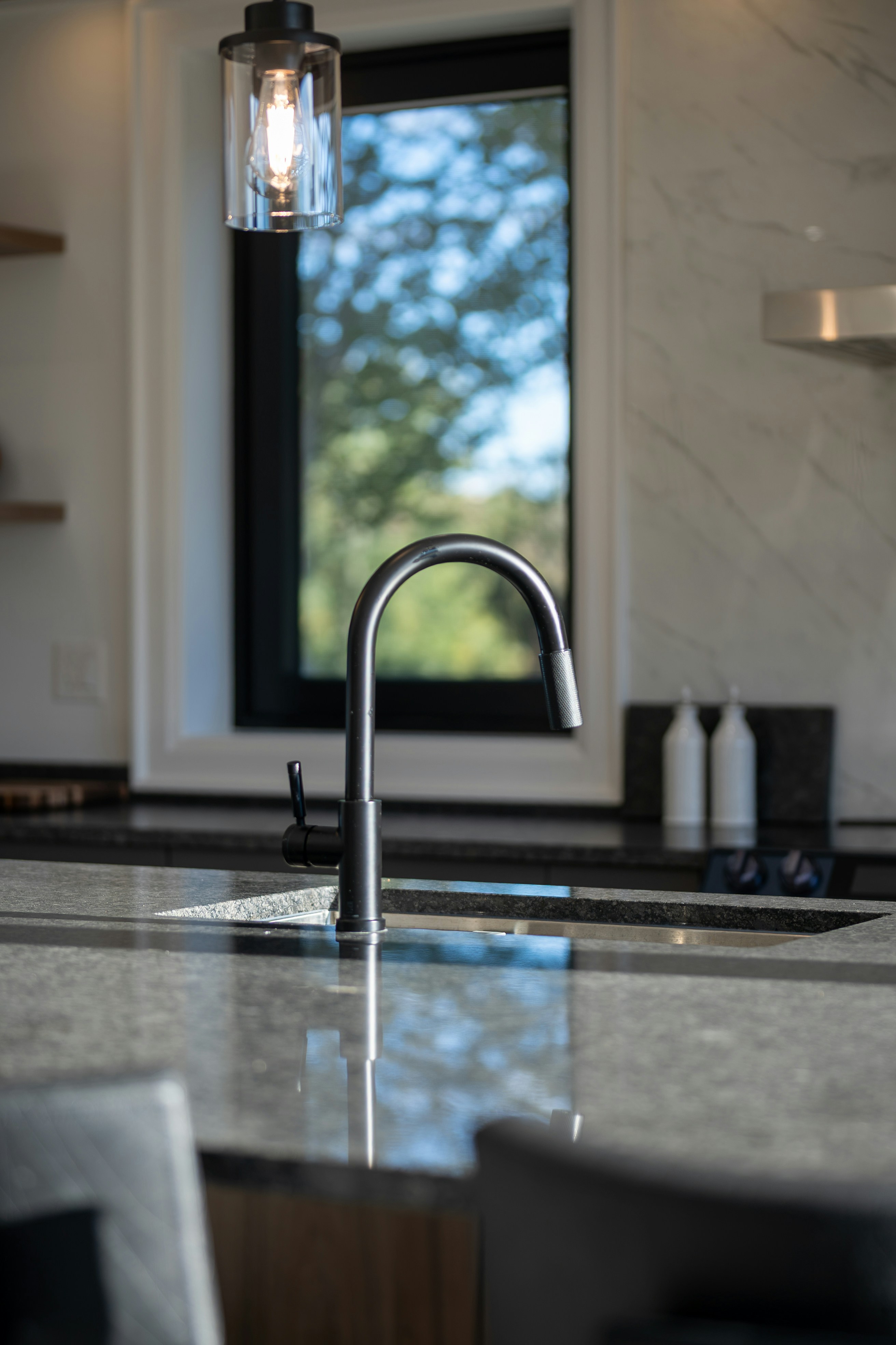 A matte black kitchen faucet on a granite island with a pendant light above