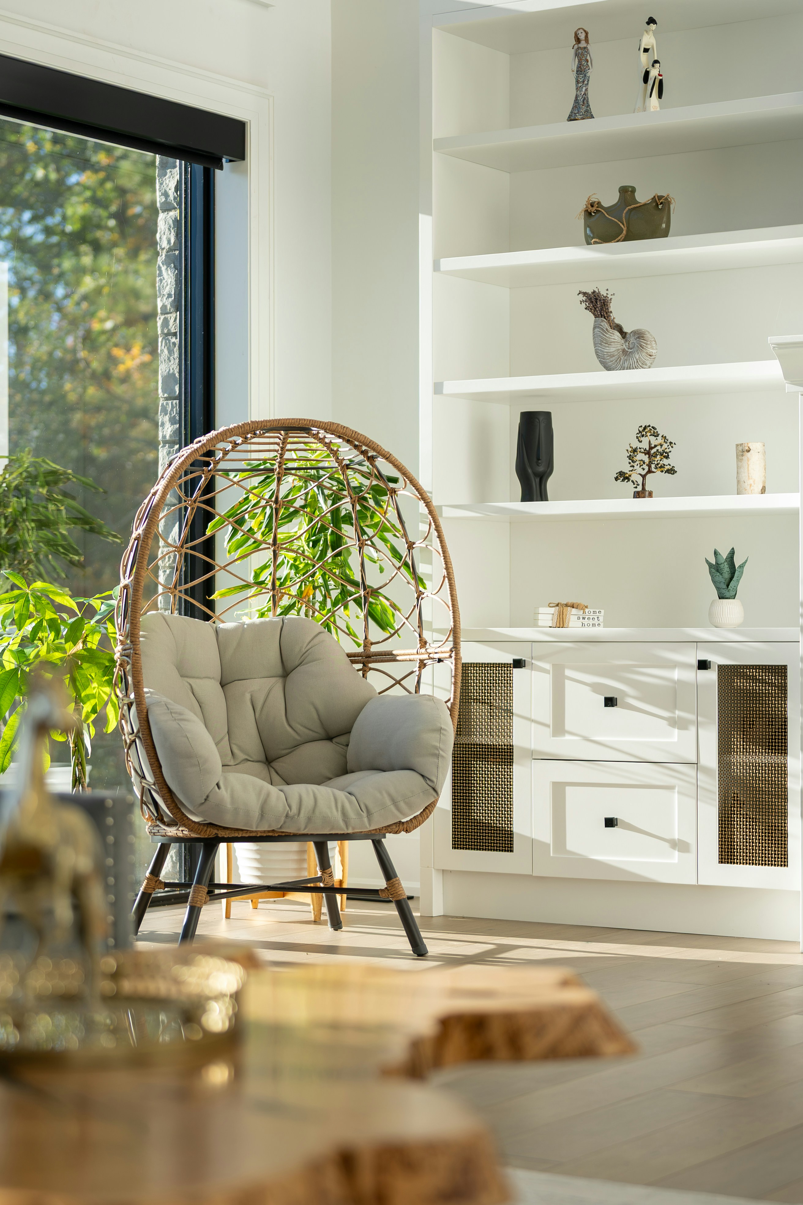 A rattan egg chair with a grey cushion in a sunlit living room