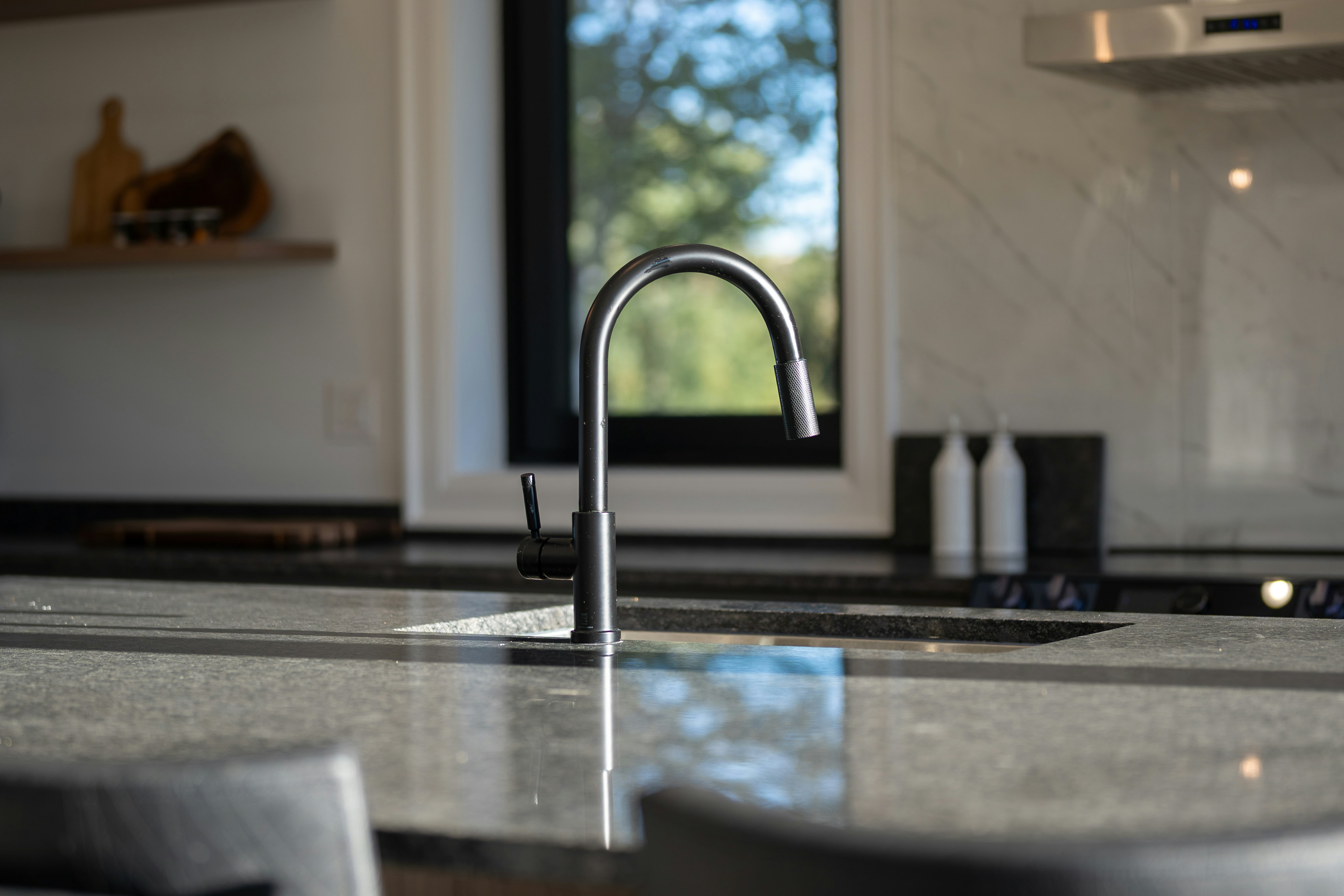 A matte black faucet over an undermount sink in a grey stone countertop