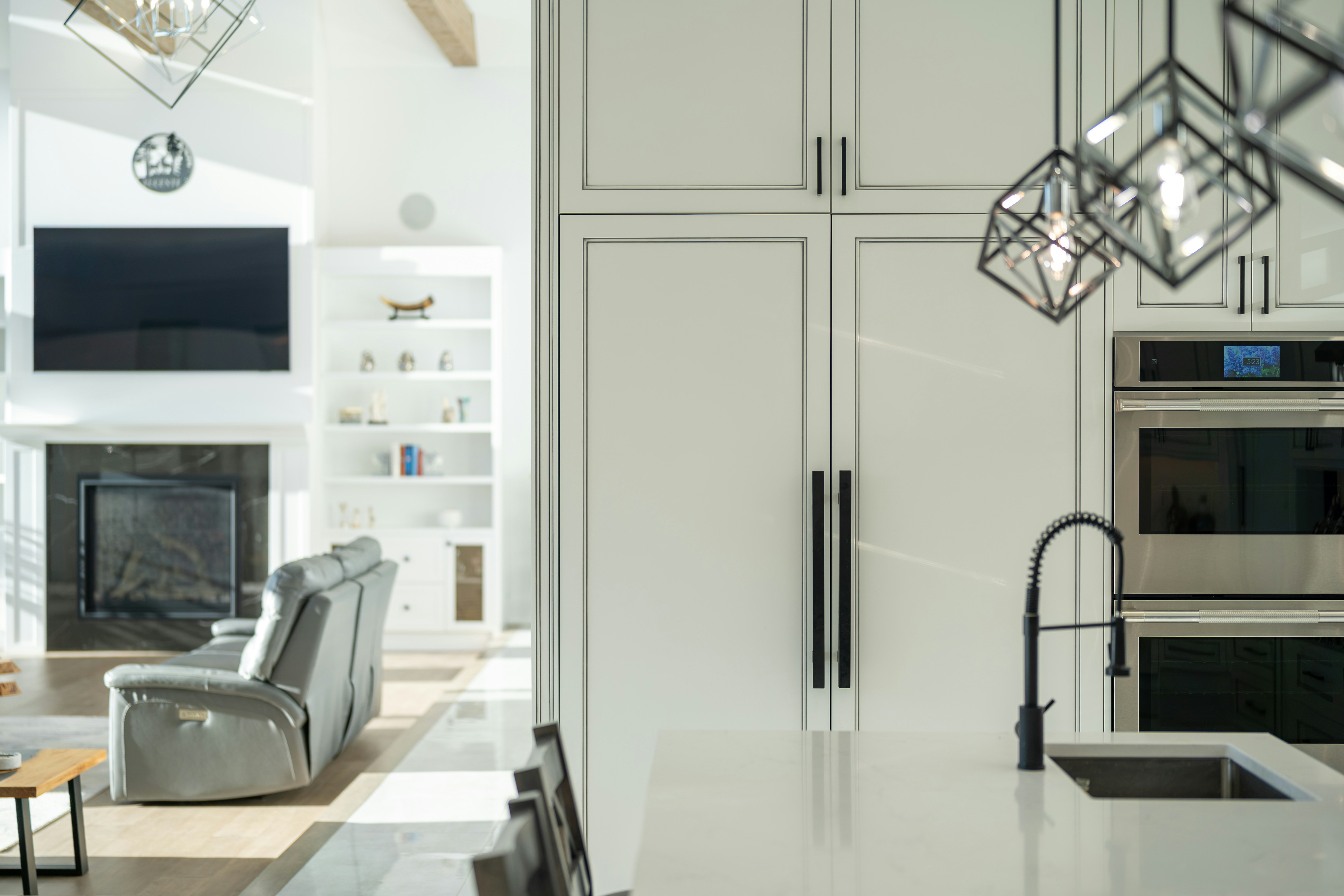 A modern kitchen with white cabinetry and a living room with a fireplace in the background