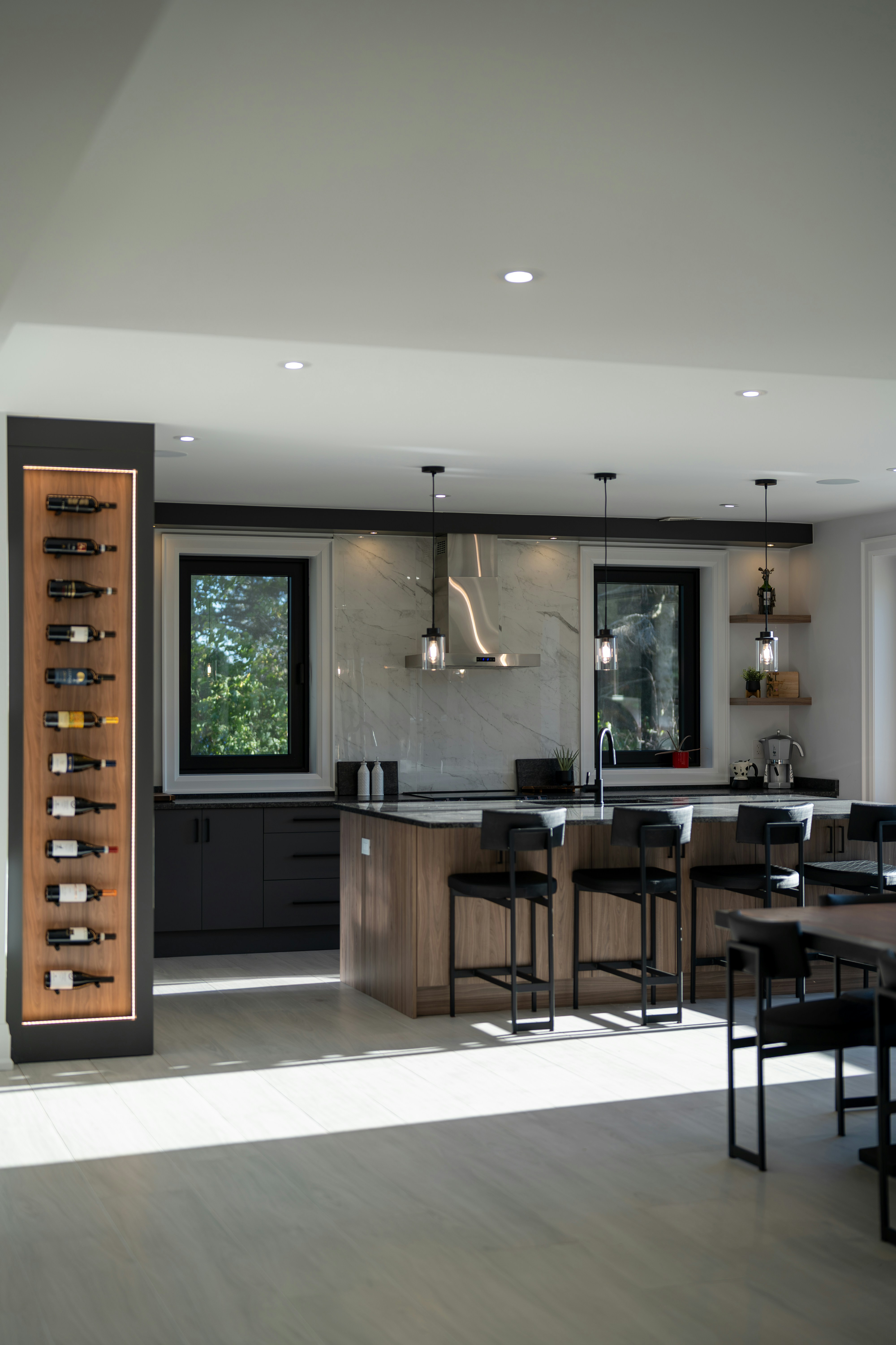 A modern kitchen with a wooden island, bar stools, and a vertical wine rack