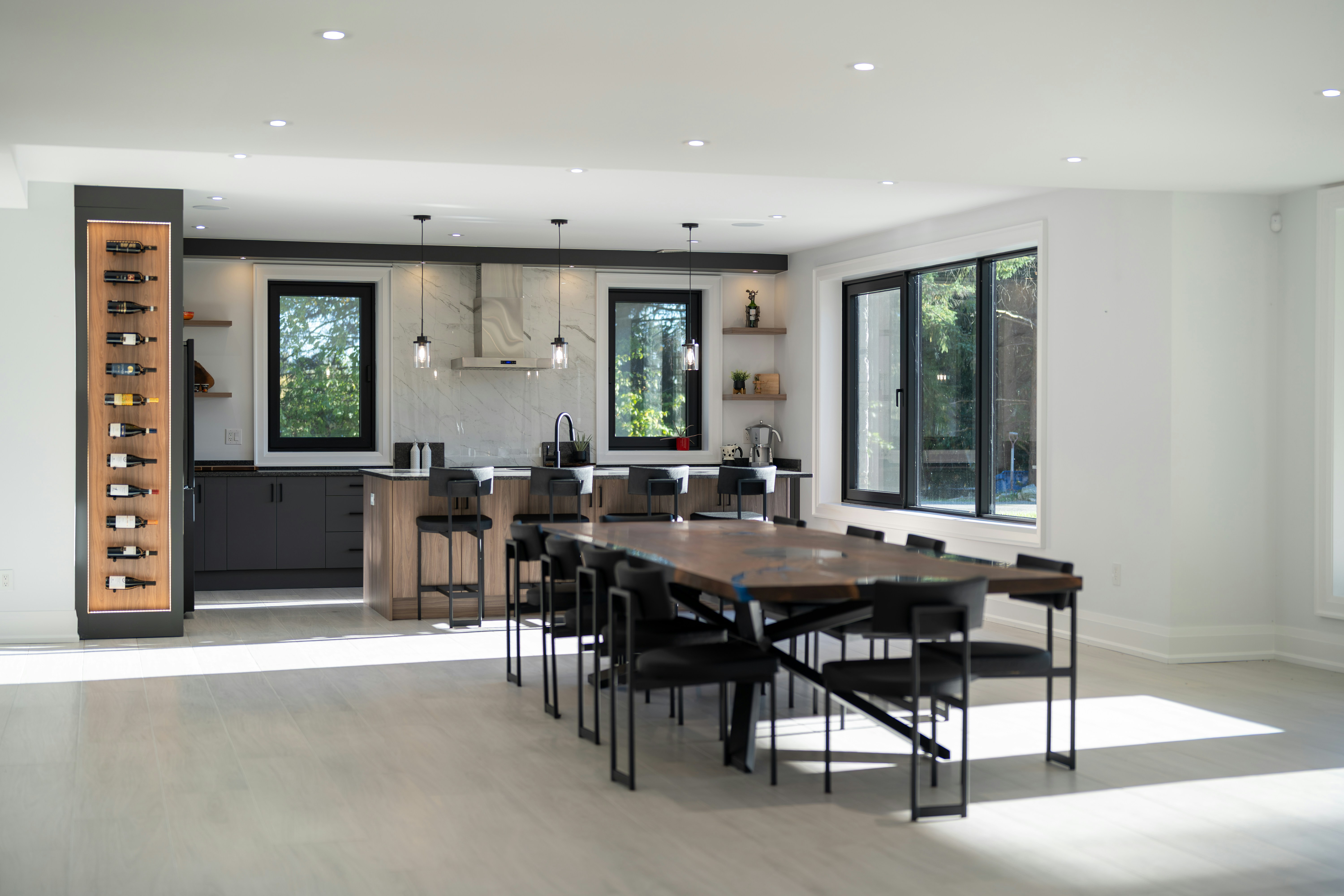 A modern kitchen with a wooden dining table, black chairs, and a vertical wine rack