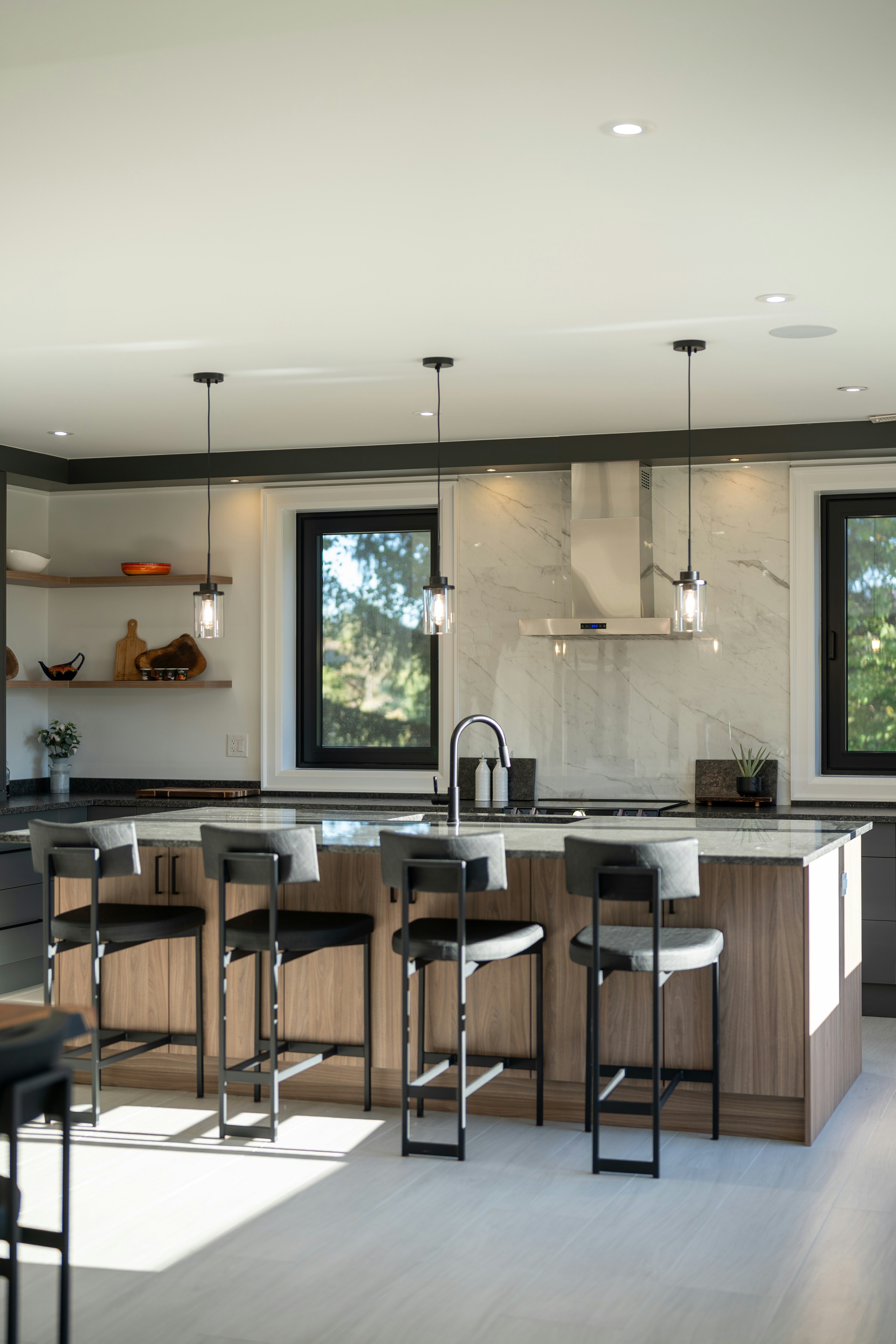 A kitchen island with four stools in front of a marble backsplash and wooden cabinets