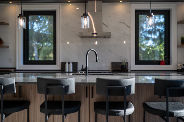 A modern kitchen island with black stools in front of a marble backsplash and