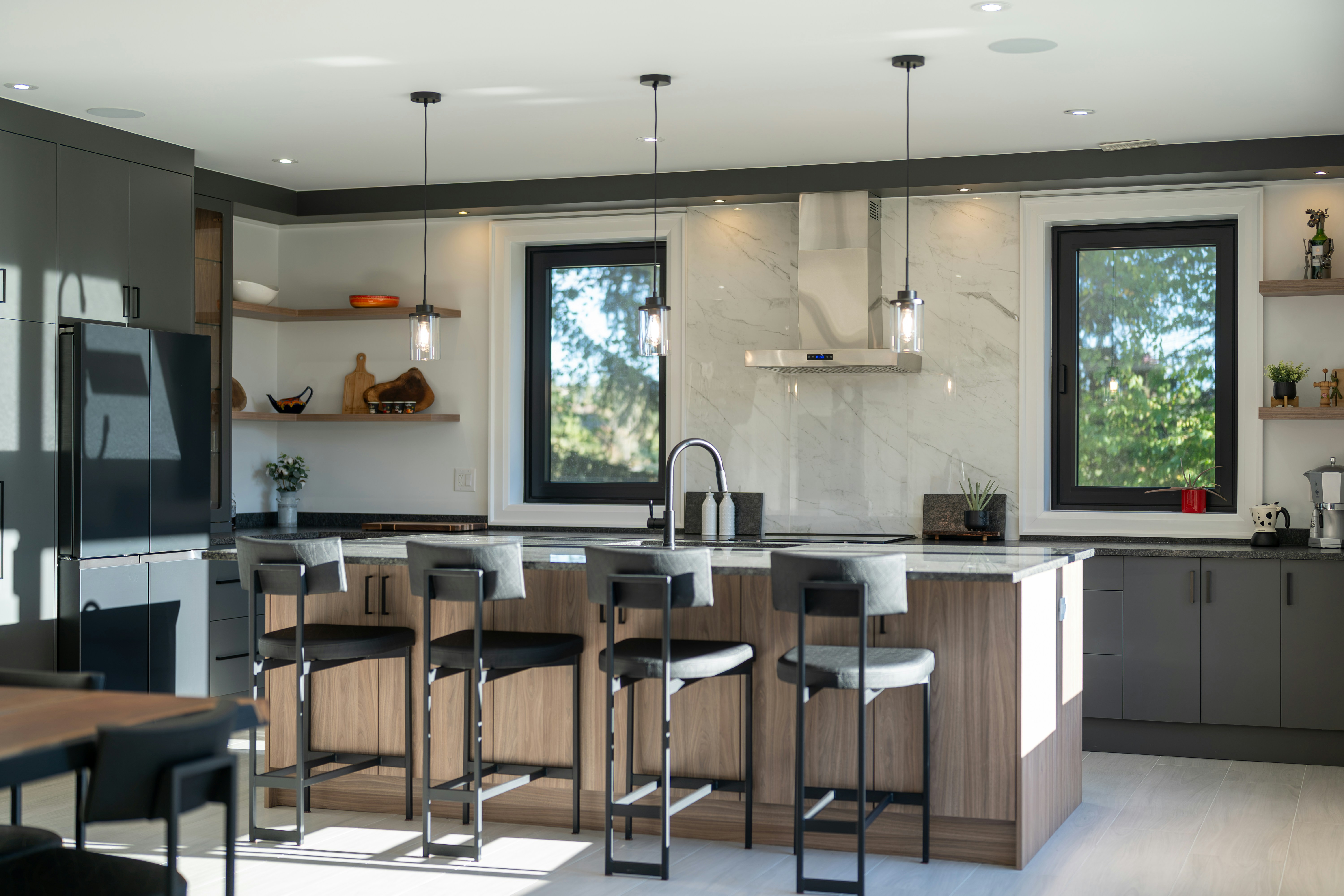 A modern kitchen with a wooden island, grey cabinets, and four bar stools in bright sunlight