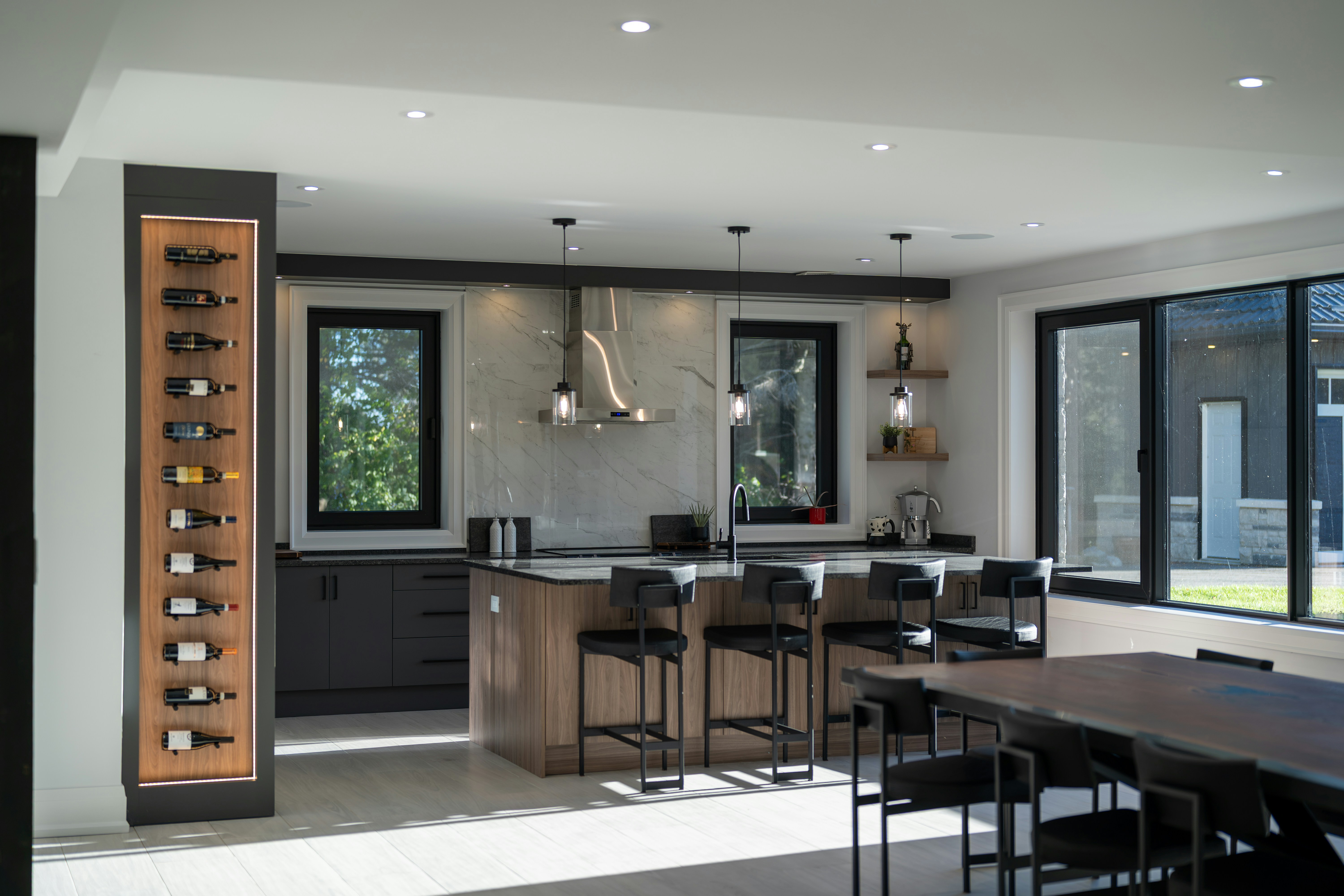 A modern kitchen with a wooden island, black bar stools, and a vertical wine rack