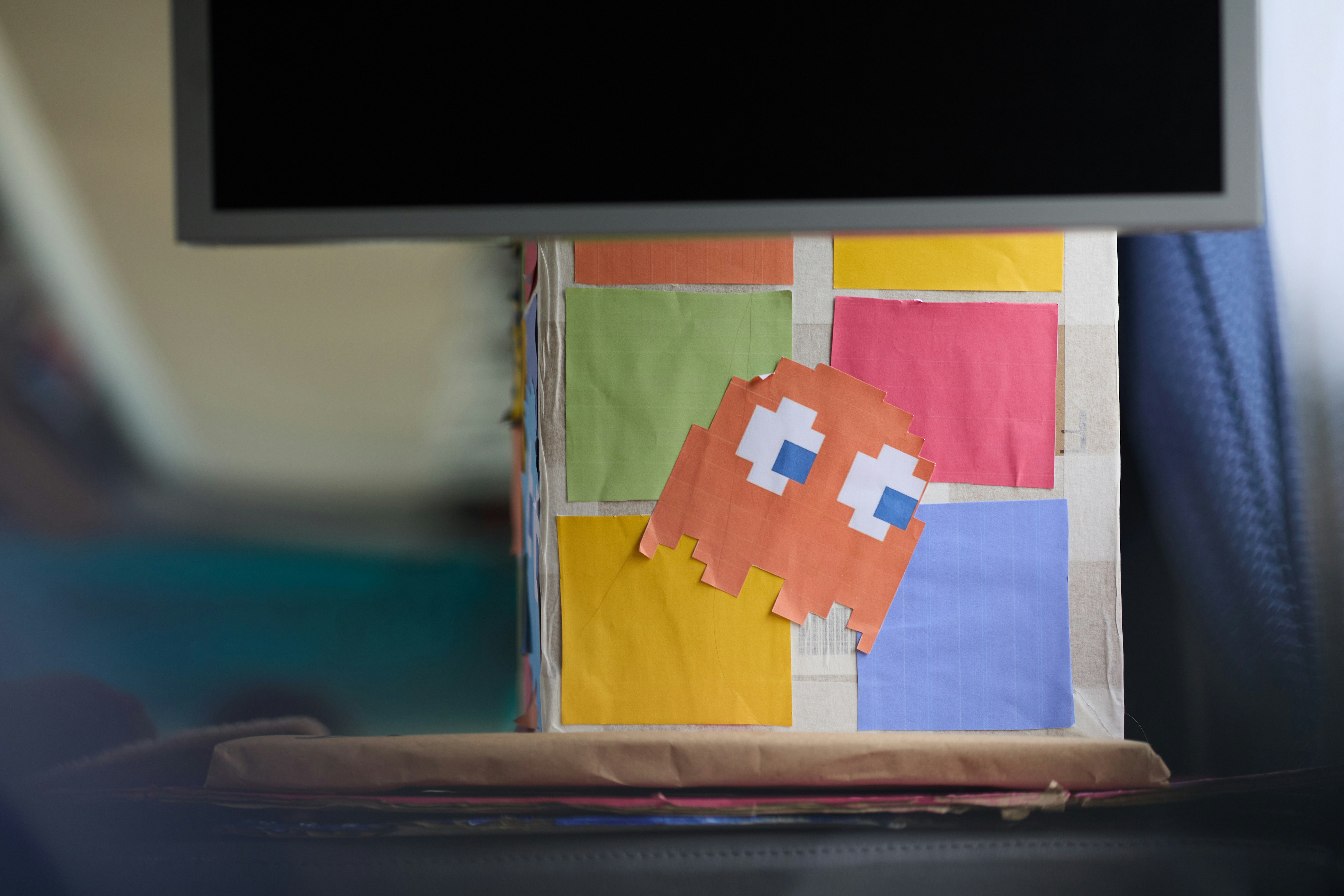A cardboard box decorated with colorful sticky notes and an orange pixelated ghost cutout