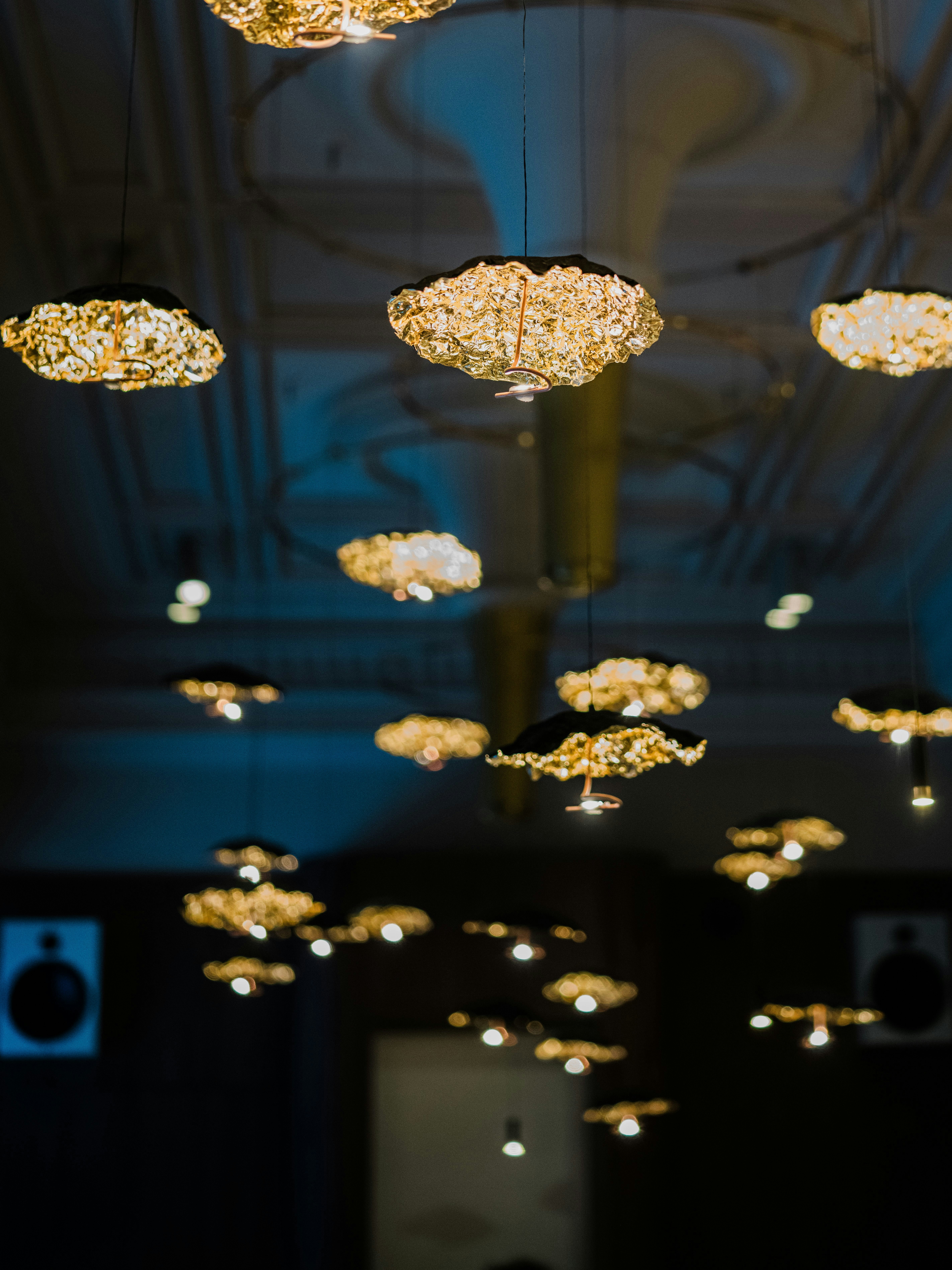 Many glowing gold textured pendant lights hanging from a dark ceiling in a dim room