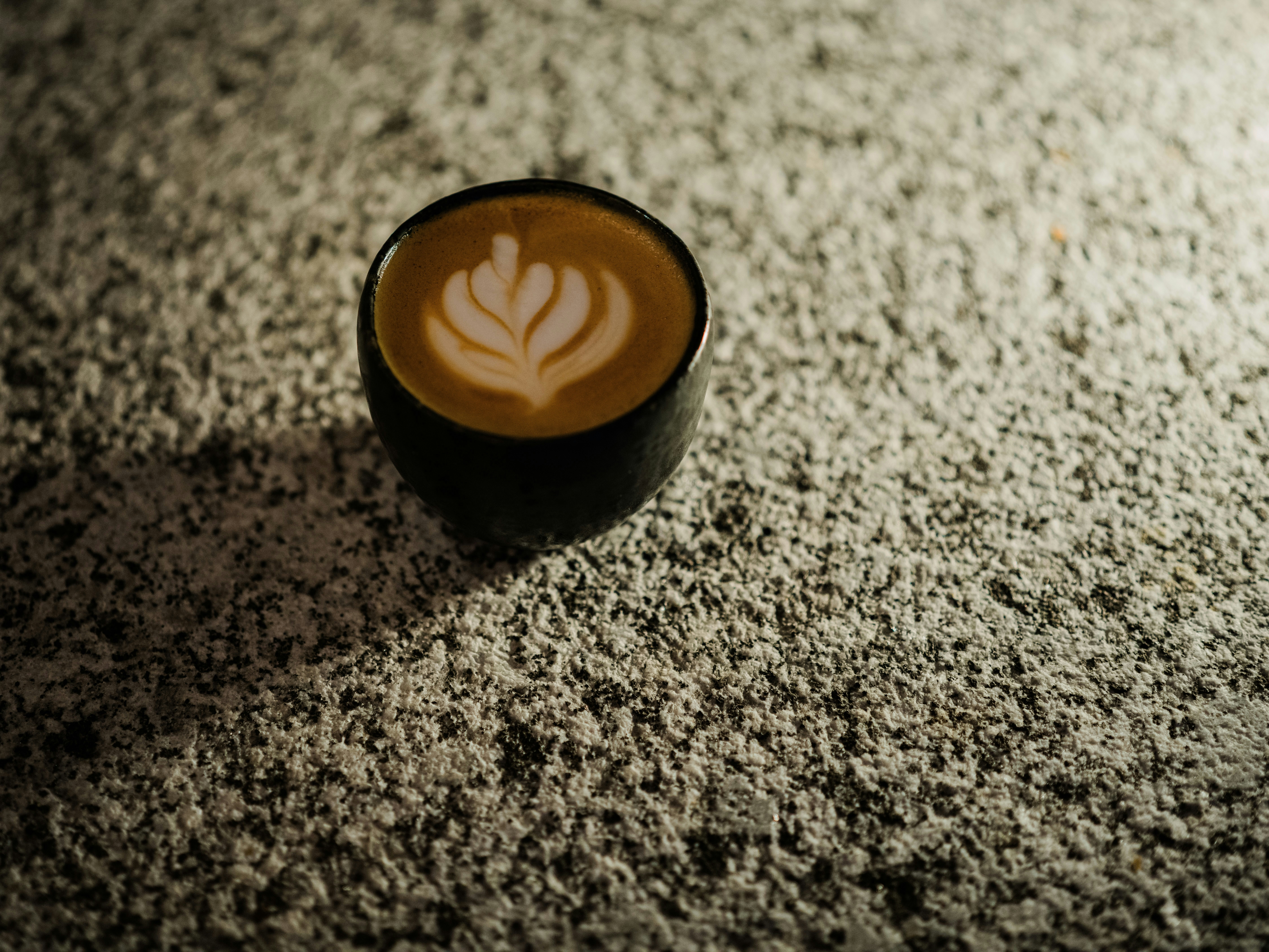 A small black cup of coffee with latte art on a textured granite surface