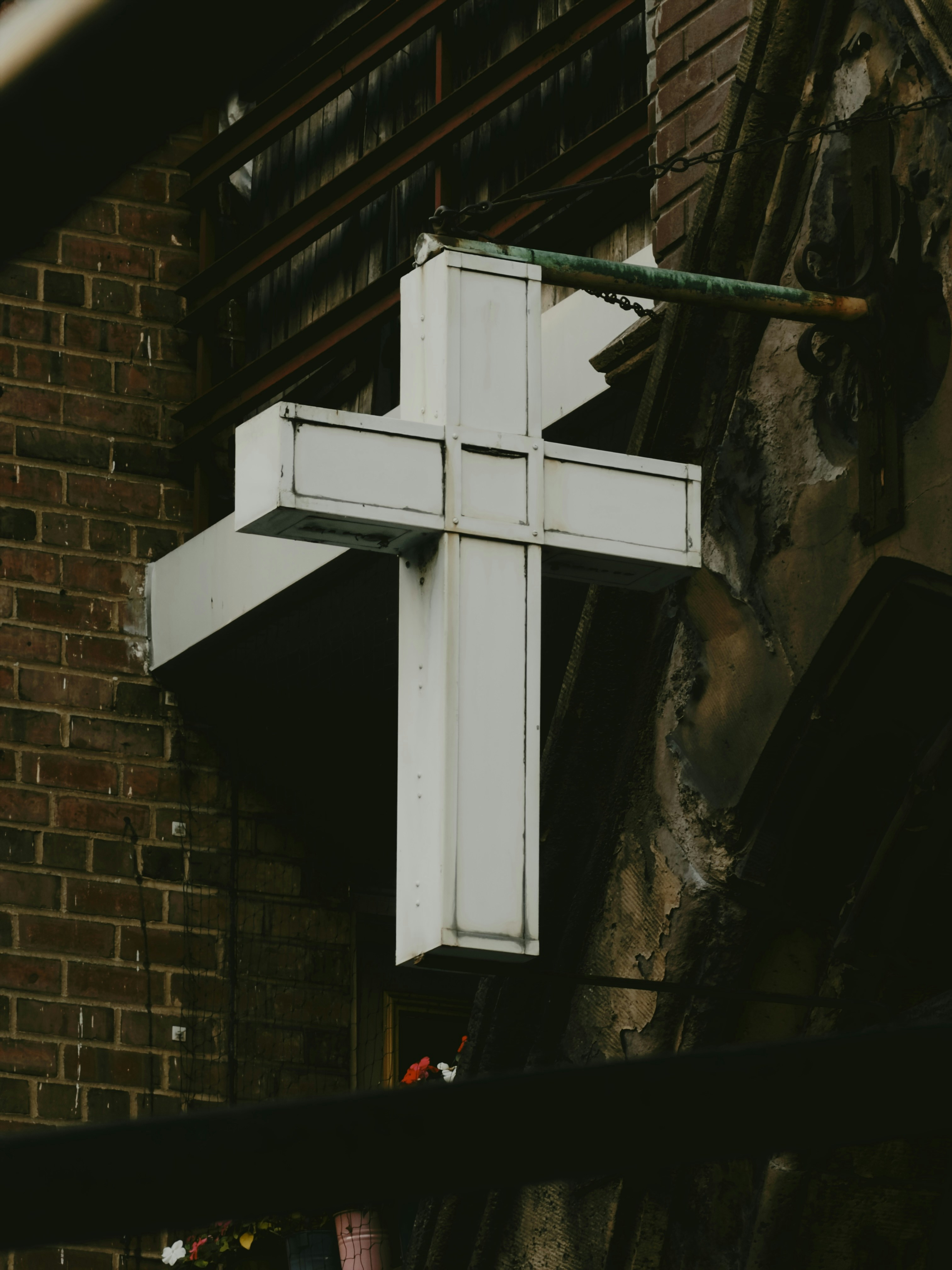 A white illuminated cross sign hanging on a weathered brick building