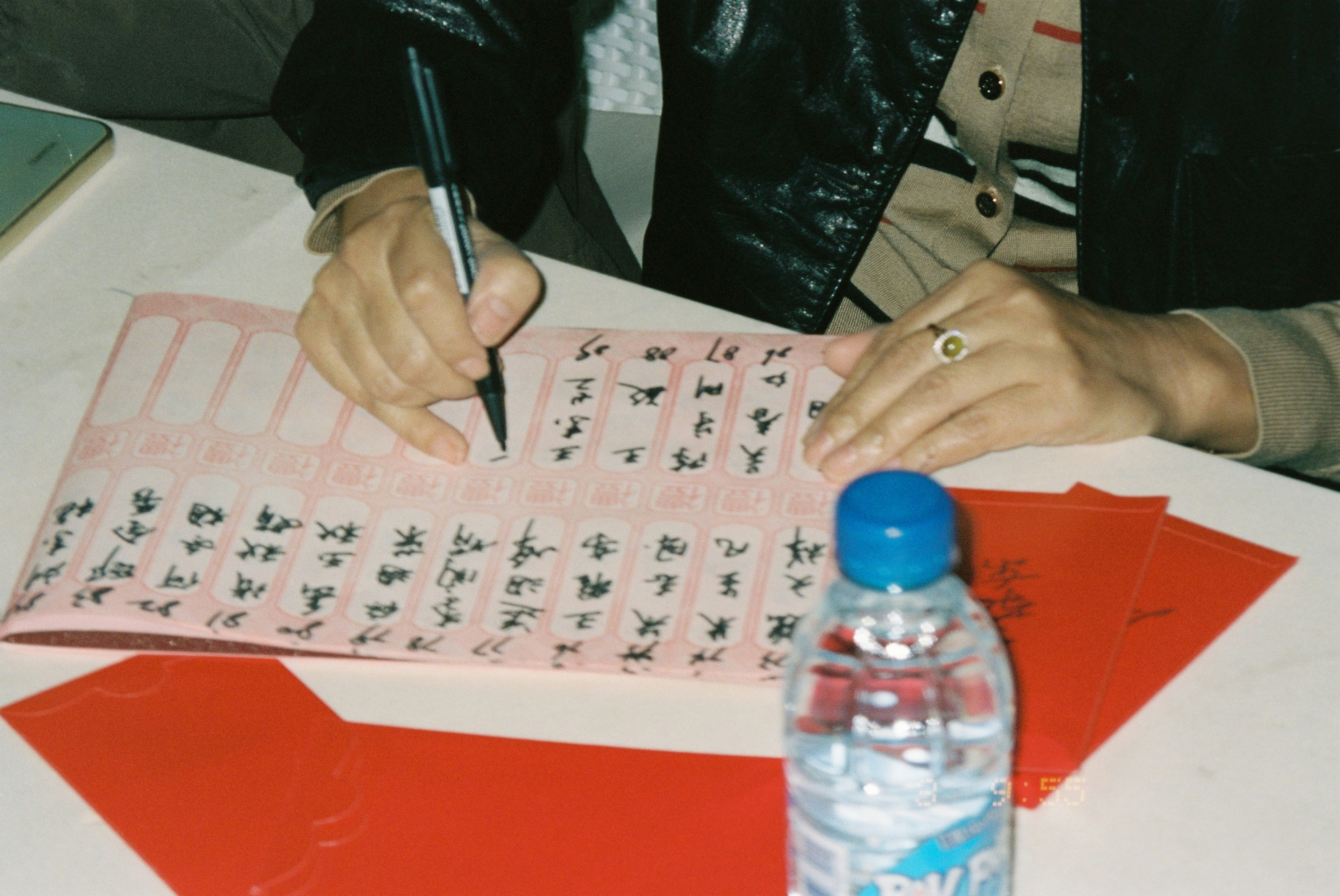 A person writing Chinese characters on a pink ledger with a black pen