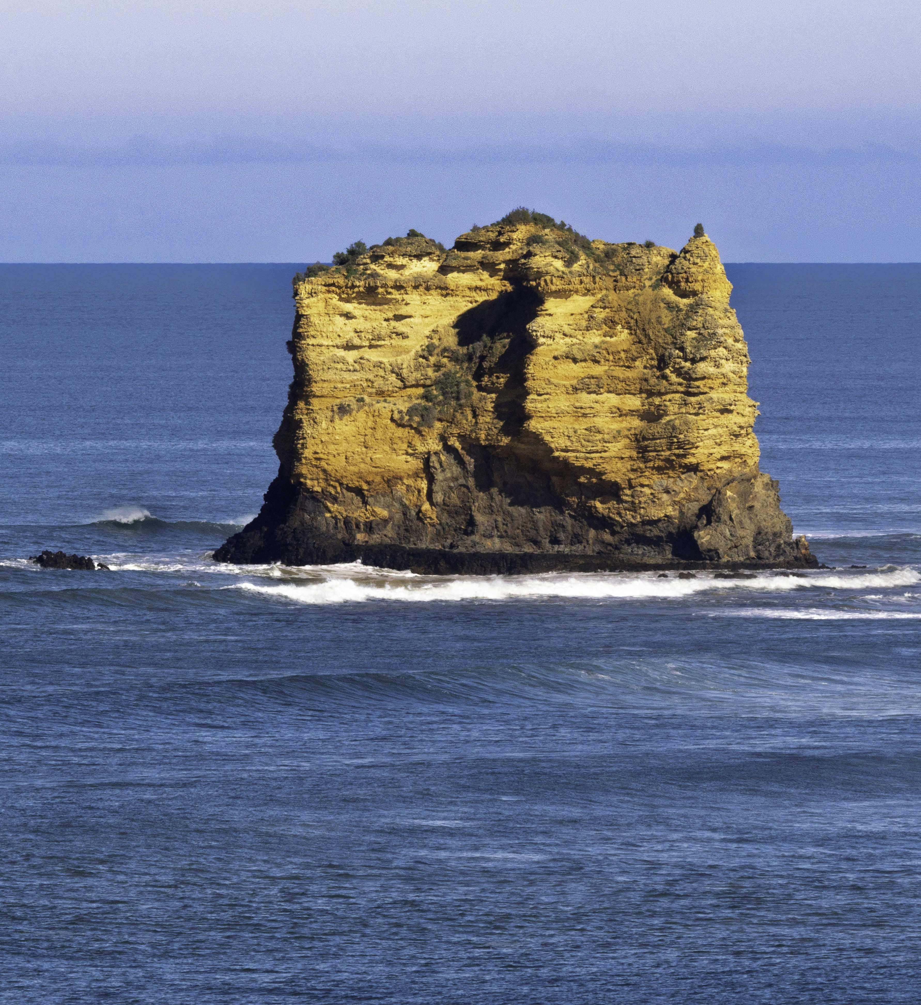 A golden sandstone sea stack rising from deep blue ocean waters