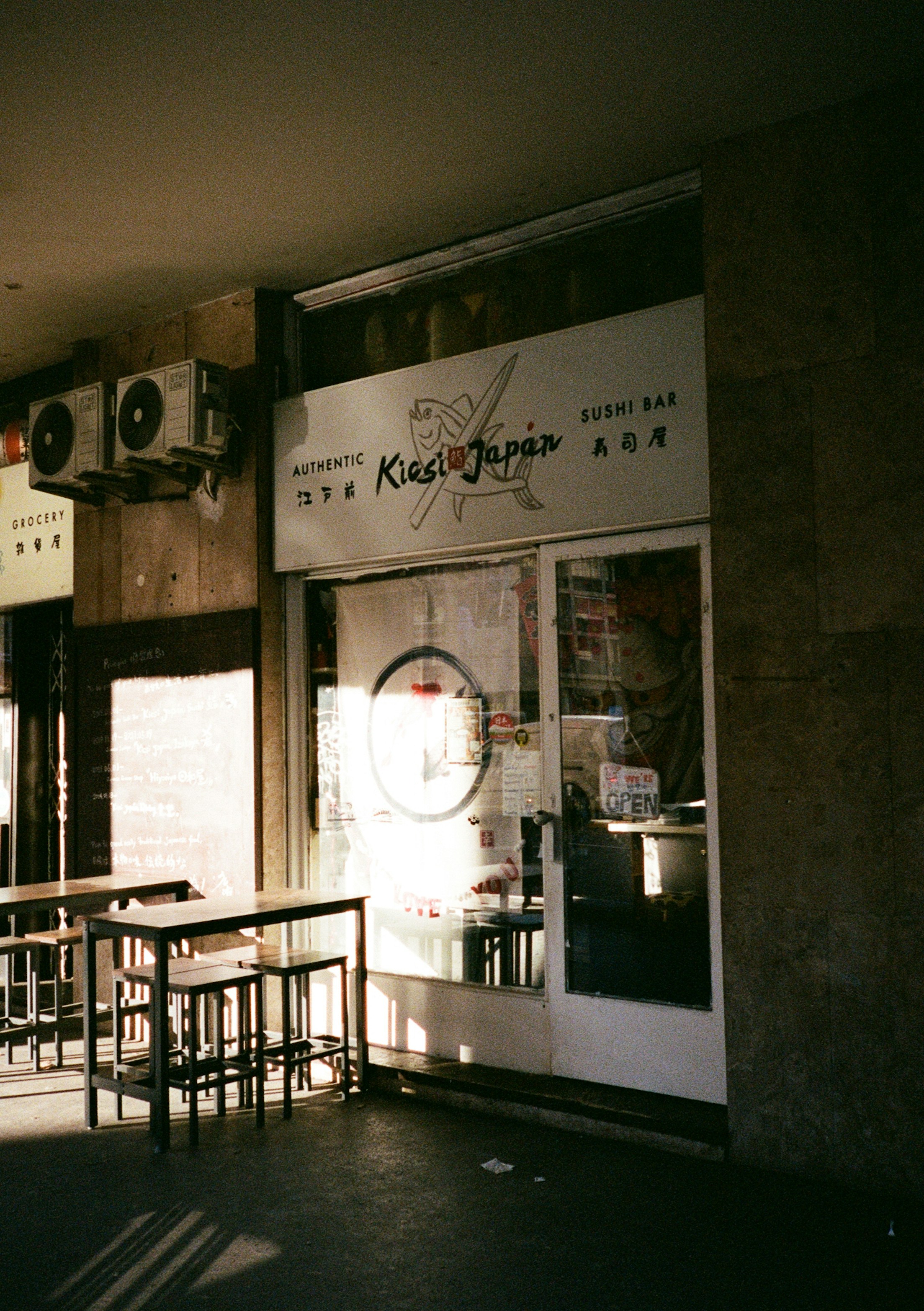 午後遅くの暖かな光の中で屋外のテーブルと椅子が並ぶ寿司バーの店先