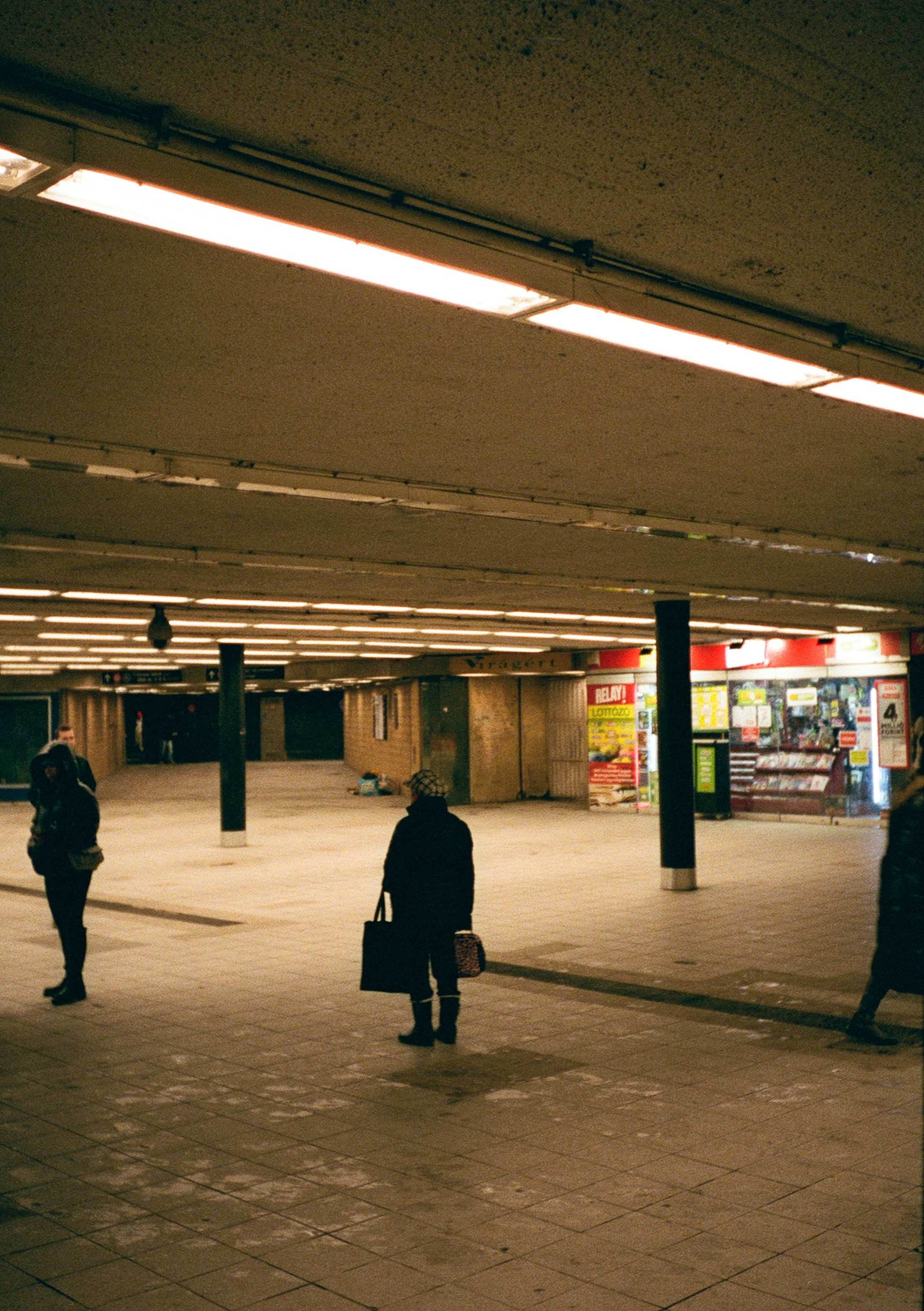 Menschen auf einem schwach beleuchteten unterirdischen Fußgängerweg in Budapest mit einem kleinen Laden im Hintergrund