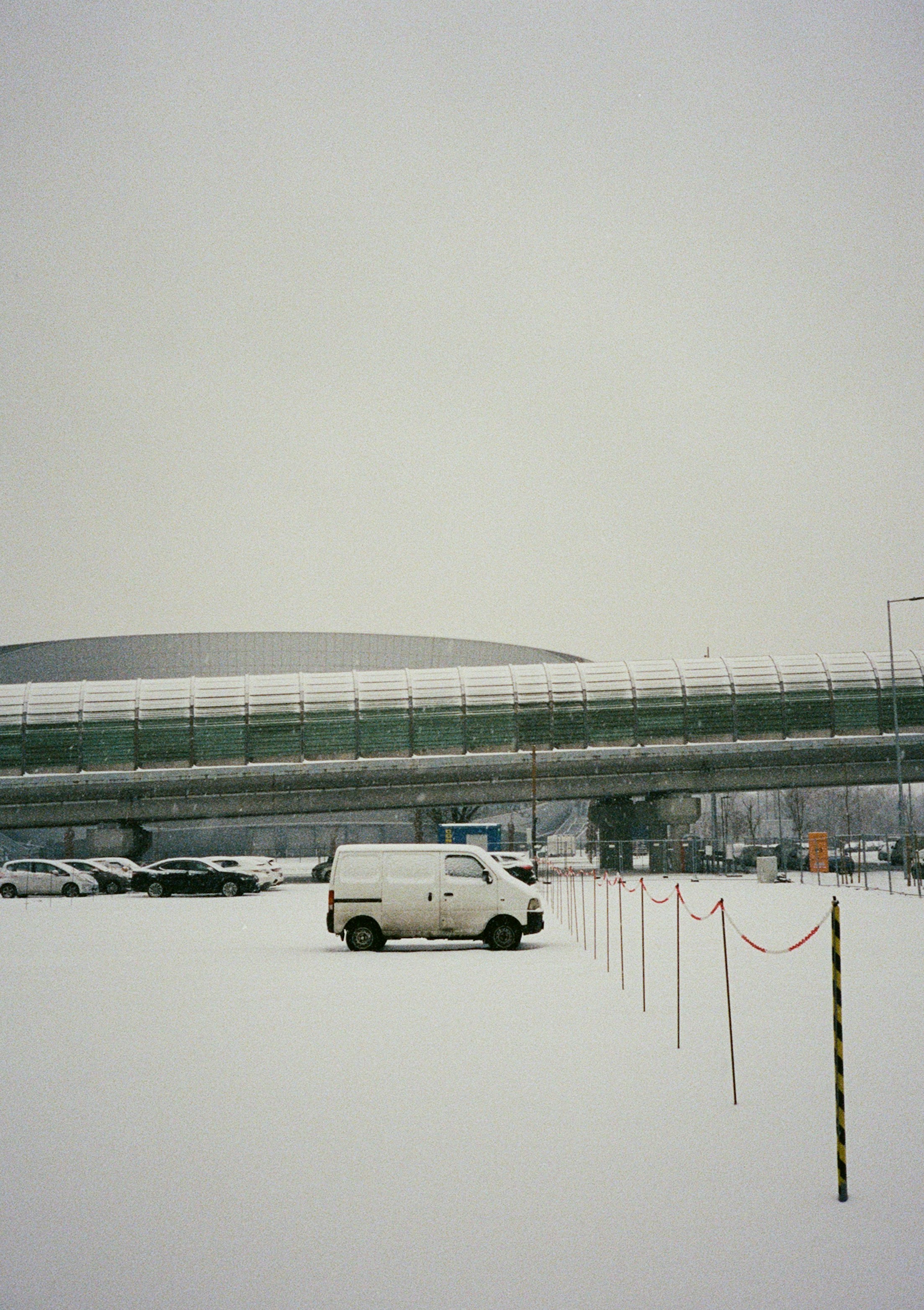 Ein weißer Van parkte auf einem schneebedeckten Parkplatz unter einem erhöhten Gehweg in Budapest