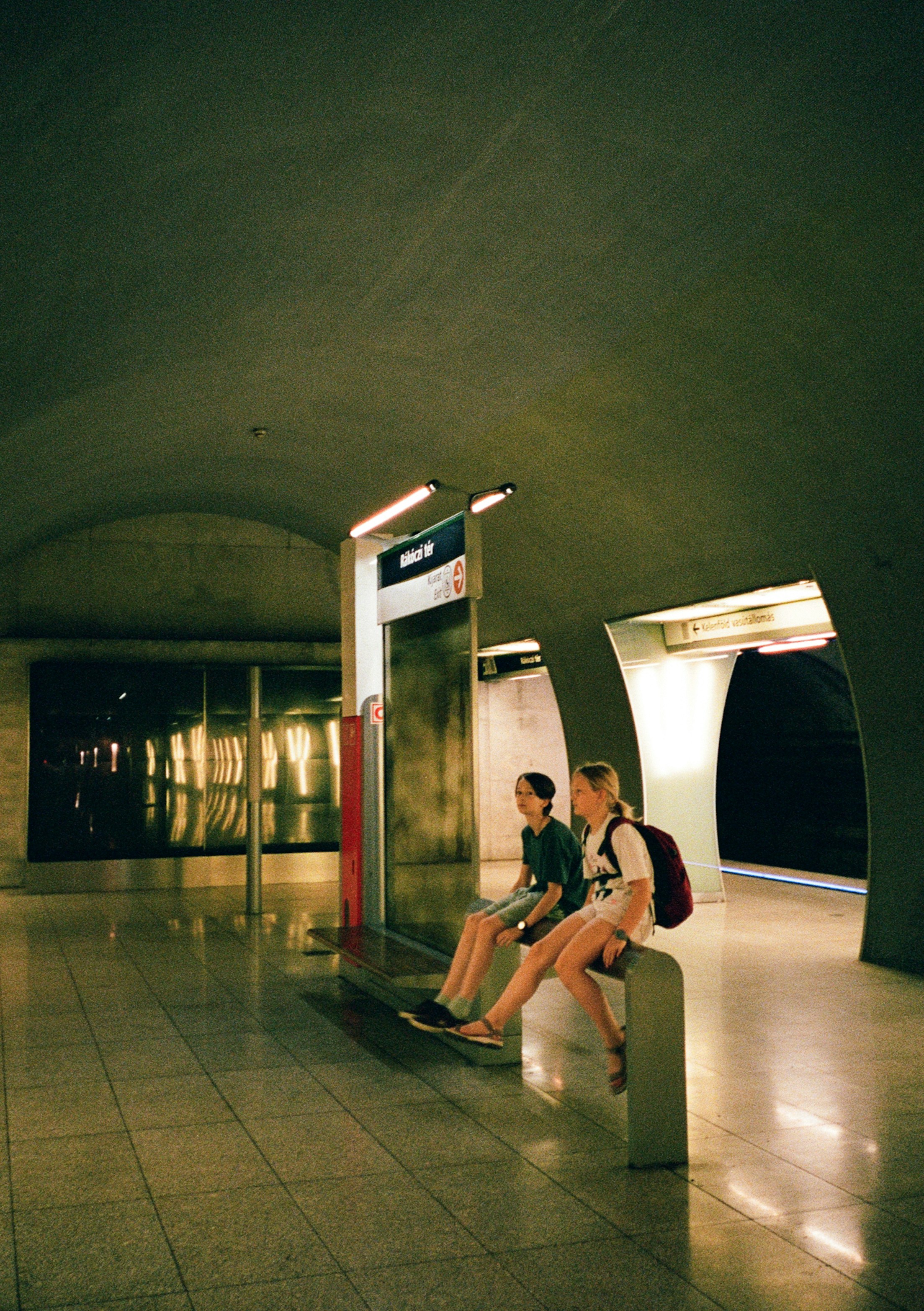 Two children sitting on a bench at the Rákóczi tér metro station in Budapest