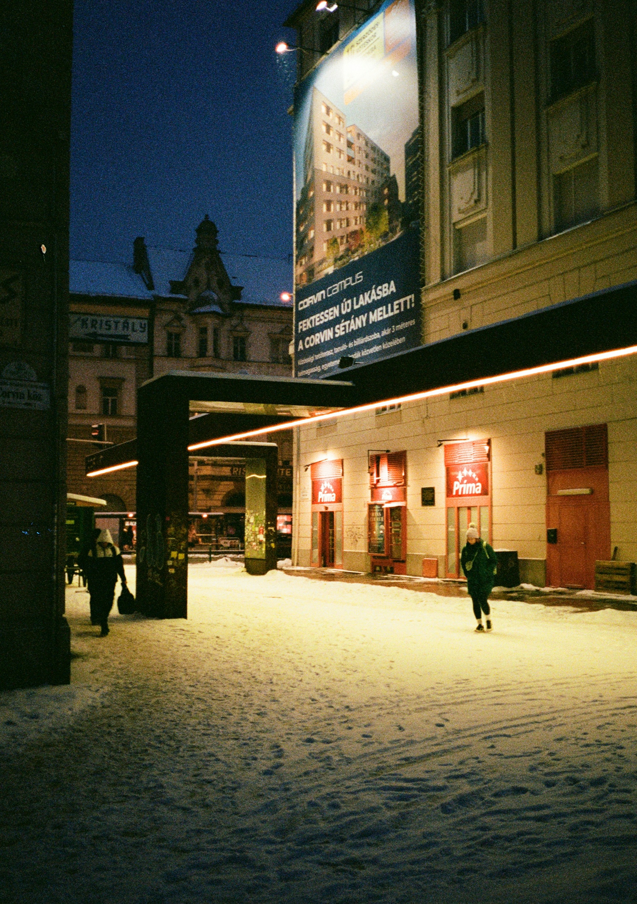 Menschen, die nachts unter warmem künstlichem Licht auf einer schneebedeckten Straße in Budapest spazieren gehen