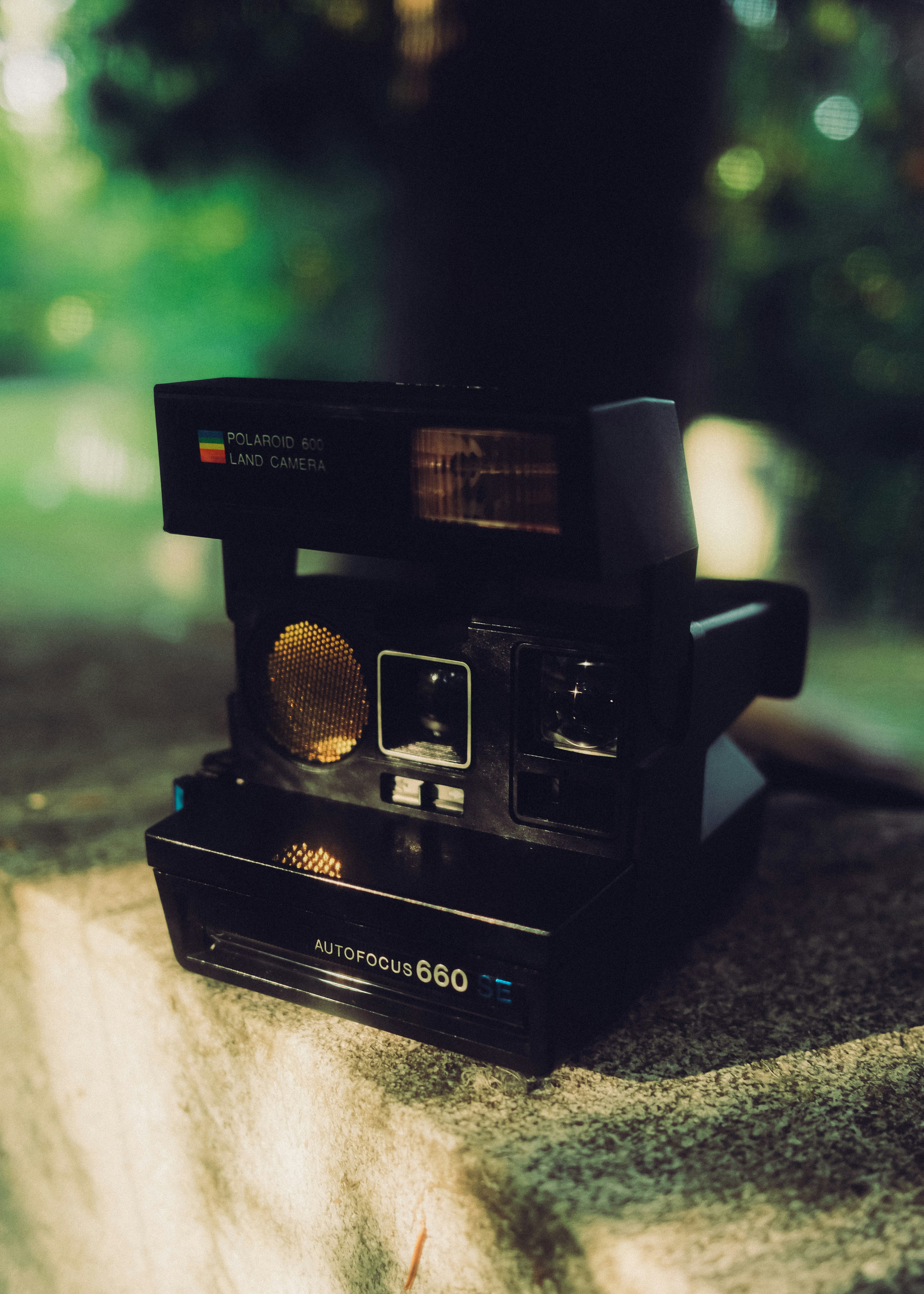 A black Polaroid 660 instant camera resting on a stone surface with a blurred green background