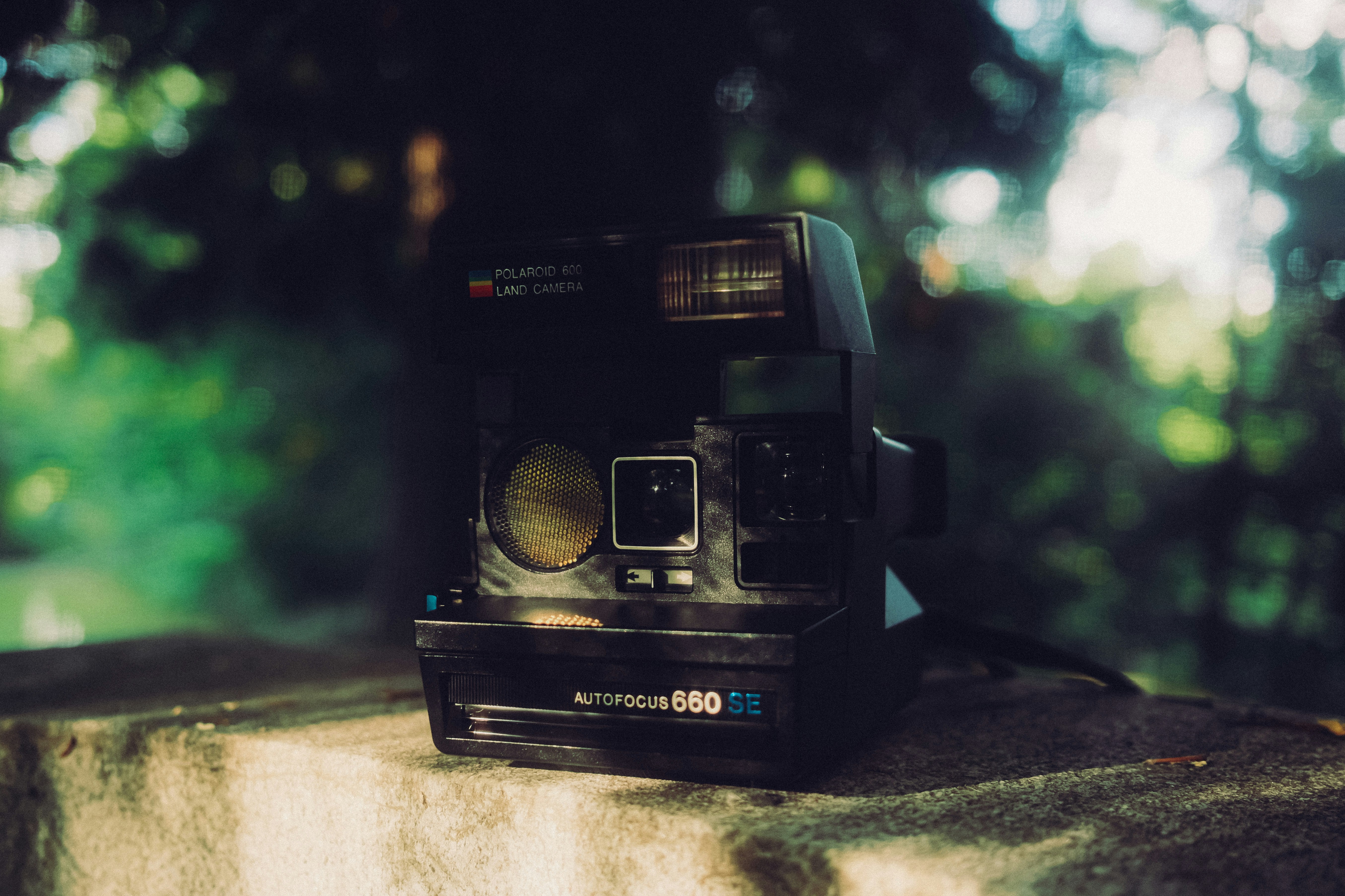 A black Polaroid 660 SE instant camera on a stone ledge with a blurred green forest background