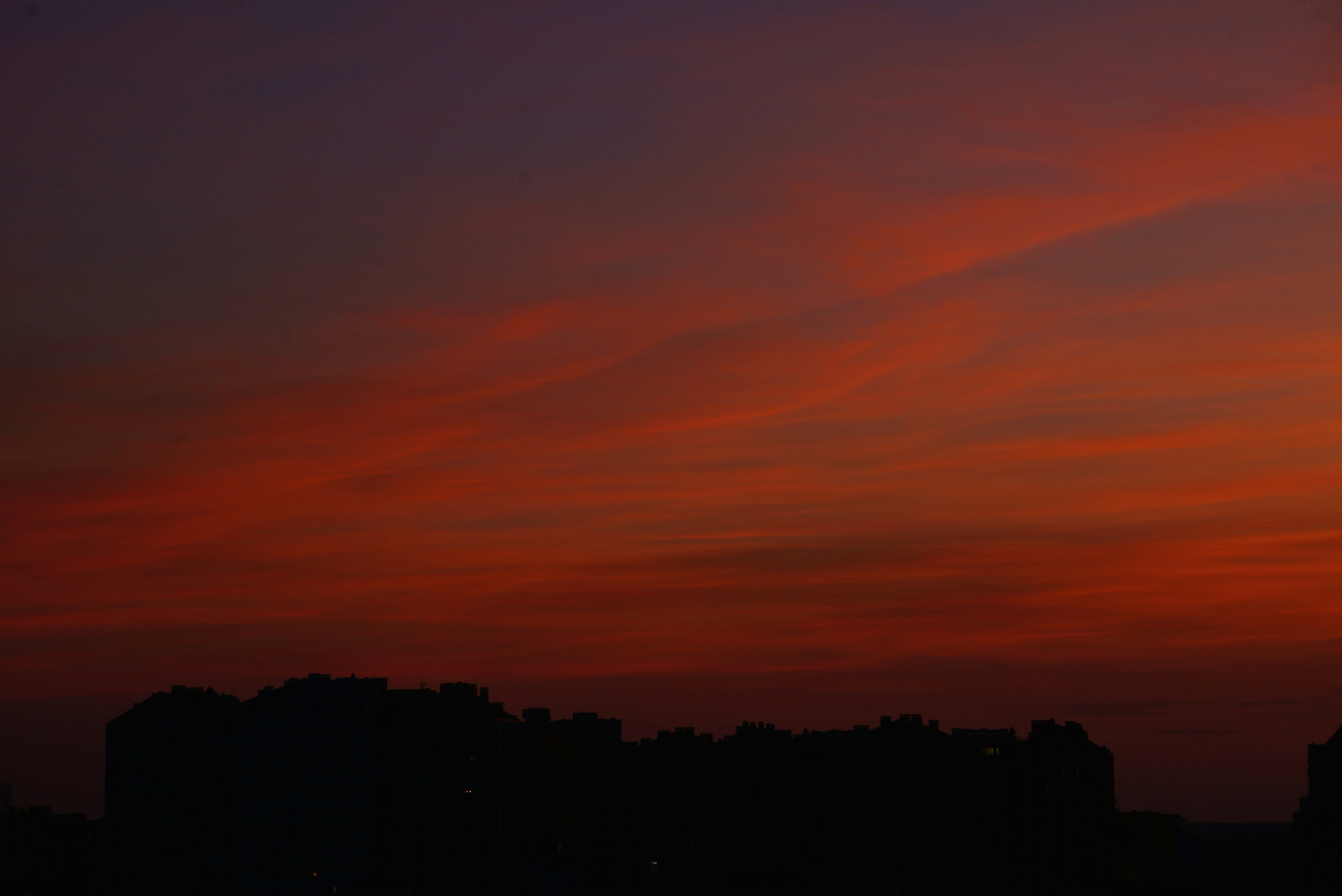 Des bâtiments citadins en silhouette sur un ciel orange vif et violet foncé