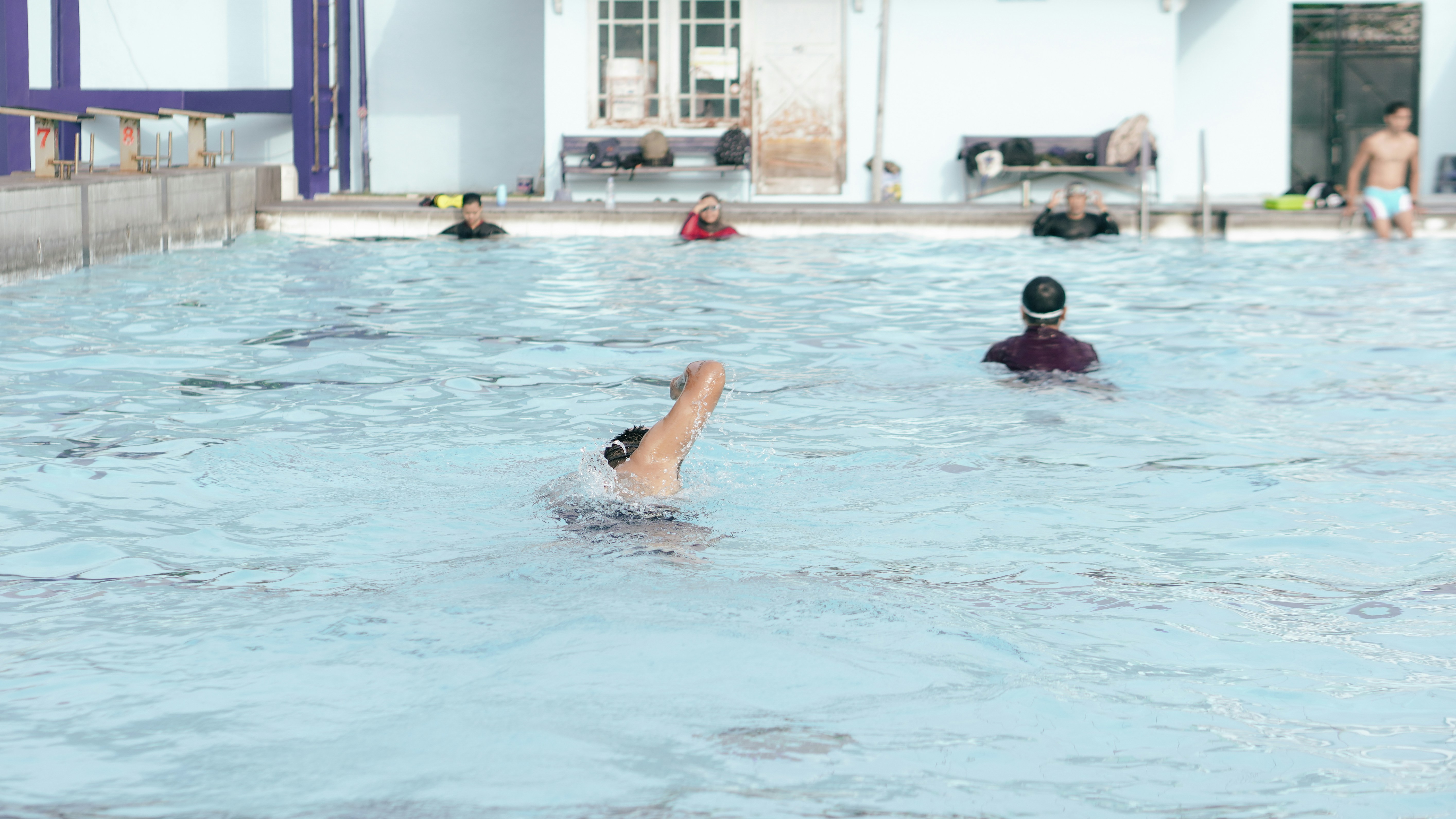 Una persona nadando en una piscina exterior luminosa con otros de fondo