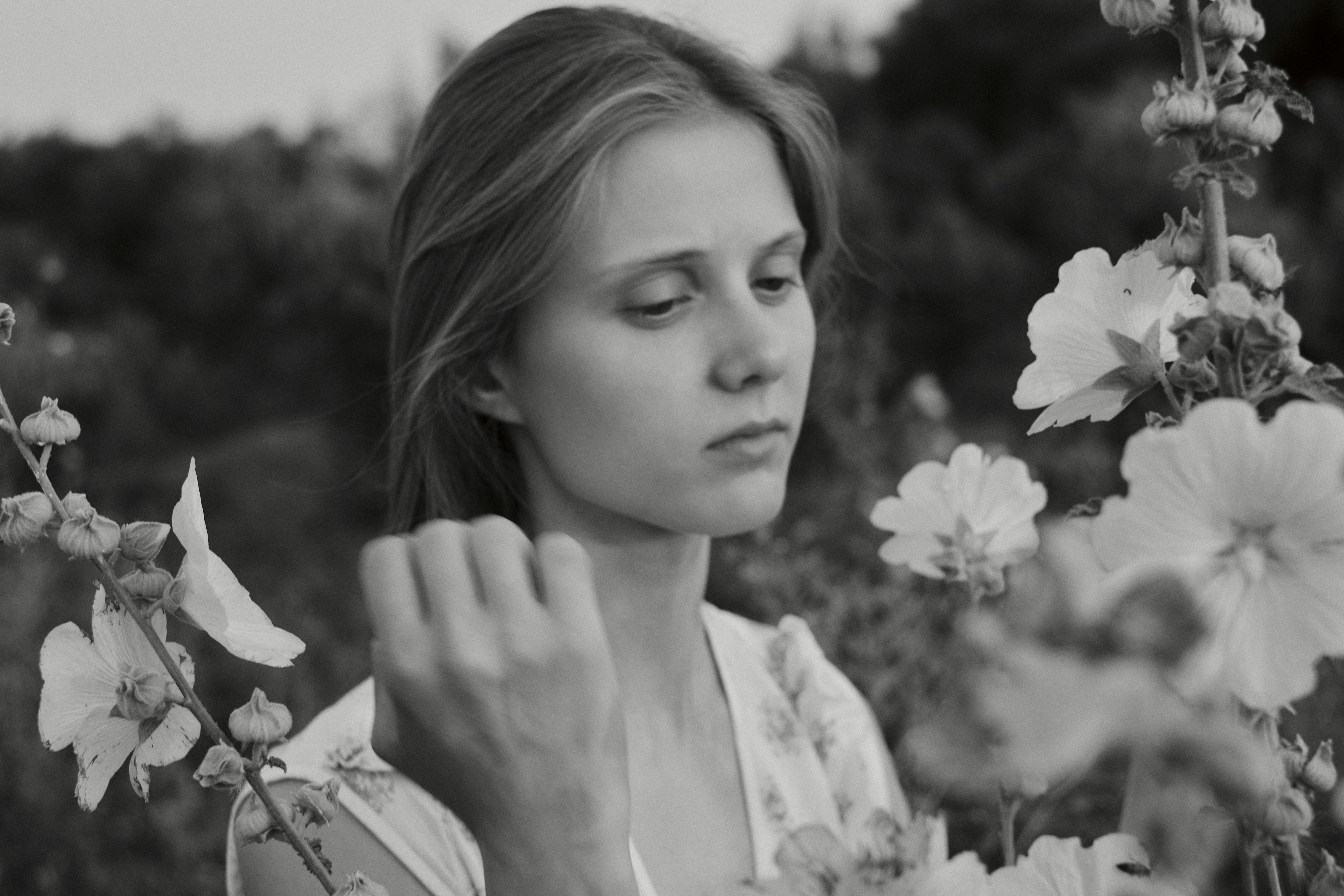 A young woman in a floral dress among tall hollyhock flowers in black and white