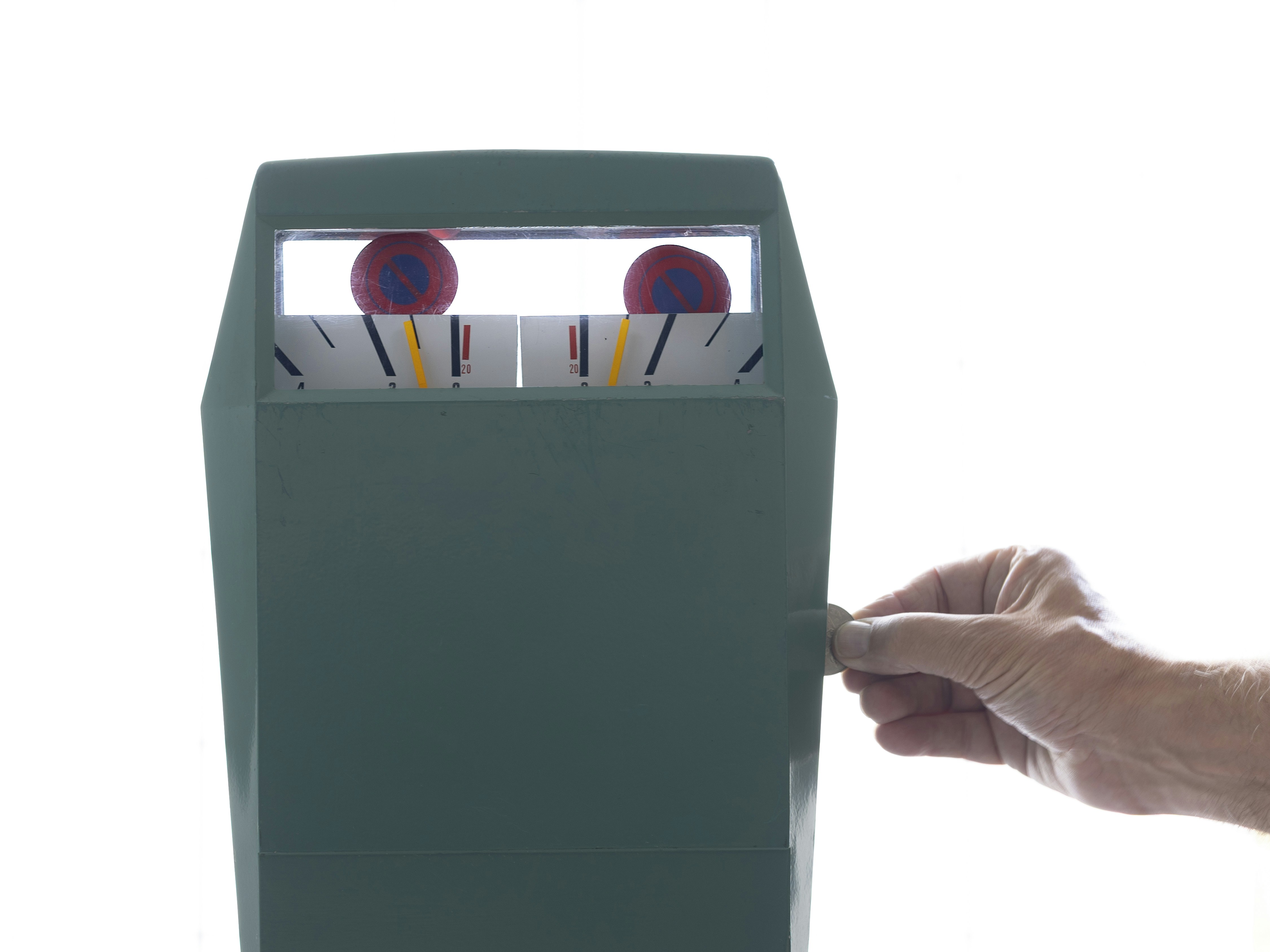 A hand inserting a coin into a green parking meter against a white background