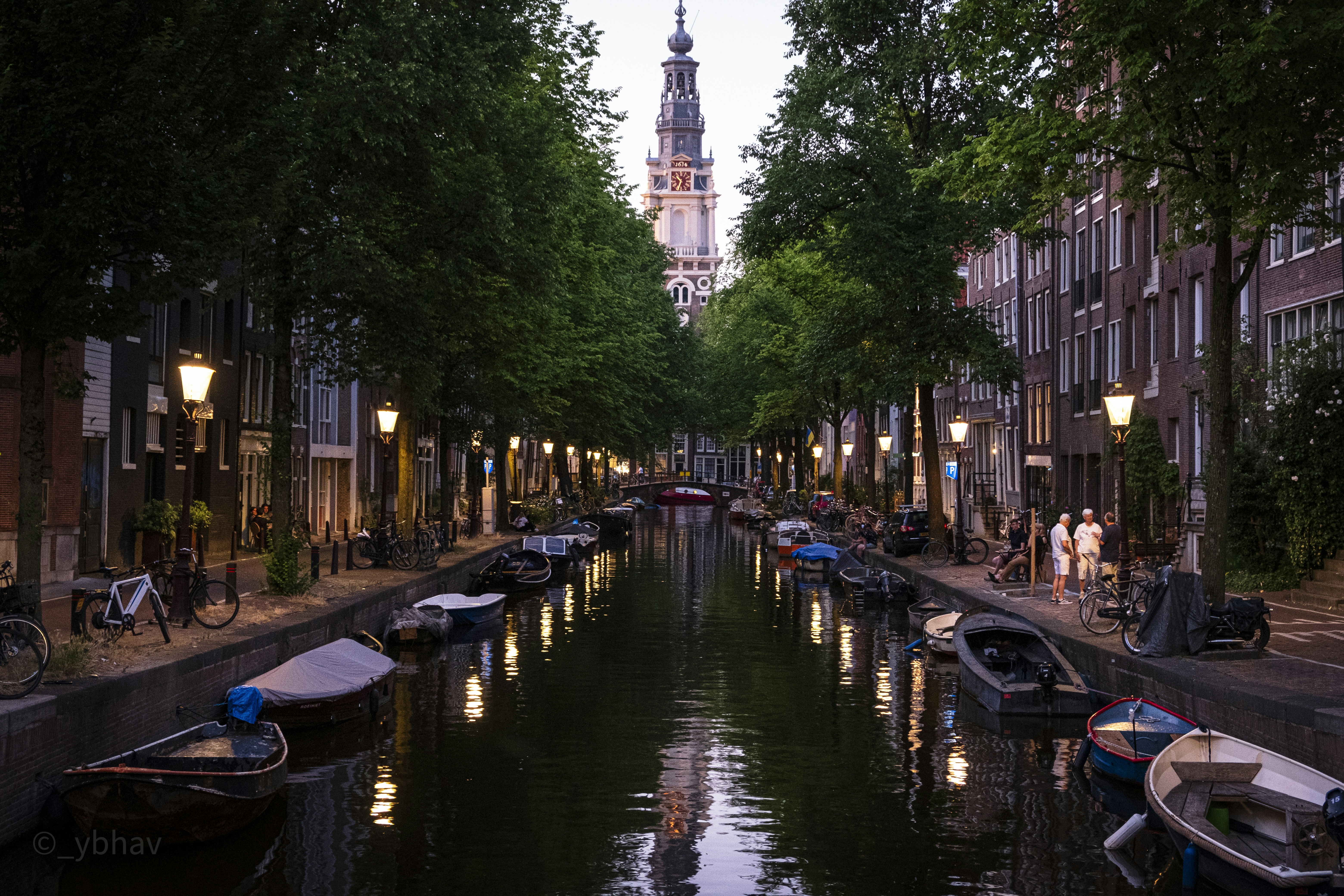 A canal in Amsterdam with moored boats and a church tower in the distance