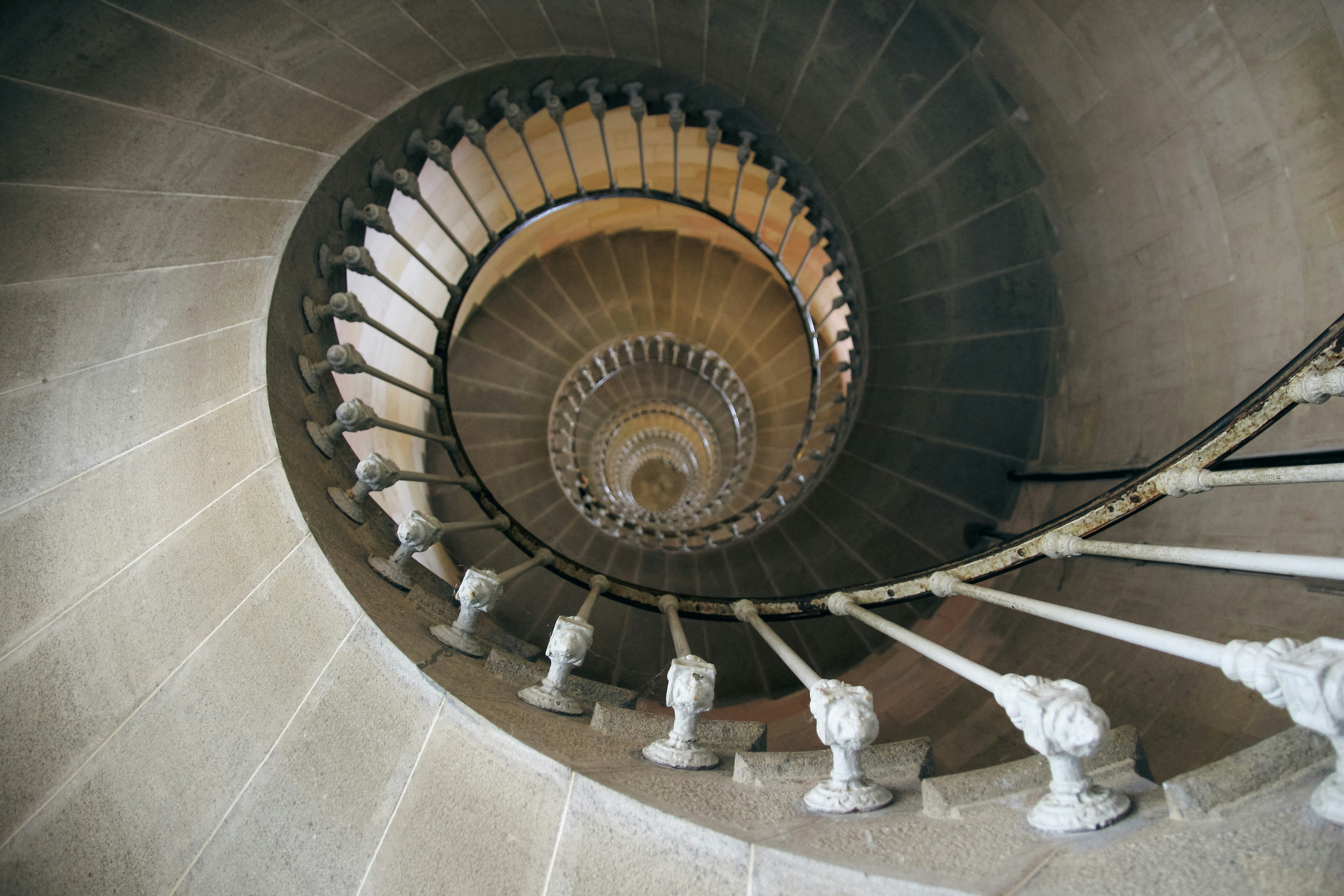 A high-angle view looking down a stone spiral staircase with a white metal railing