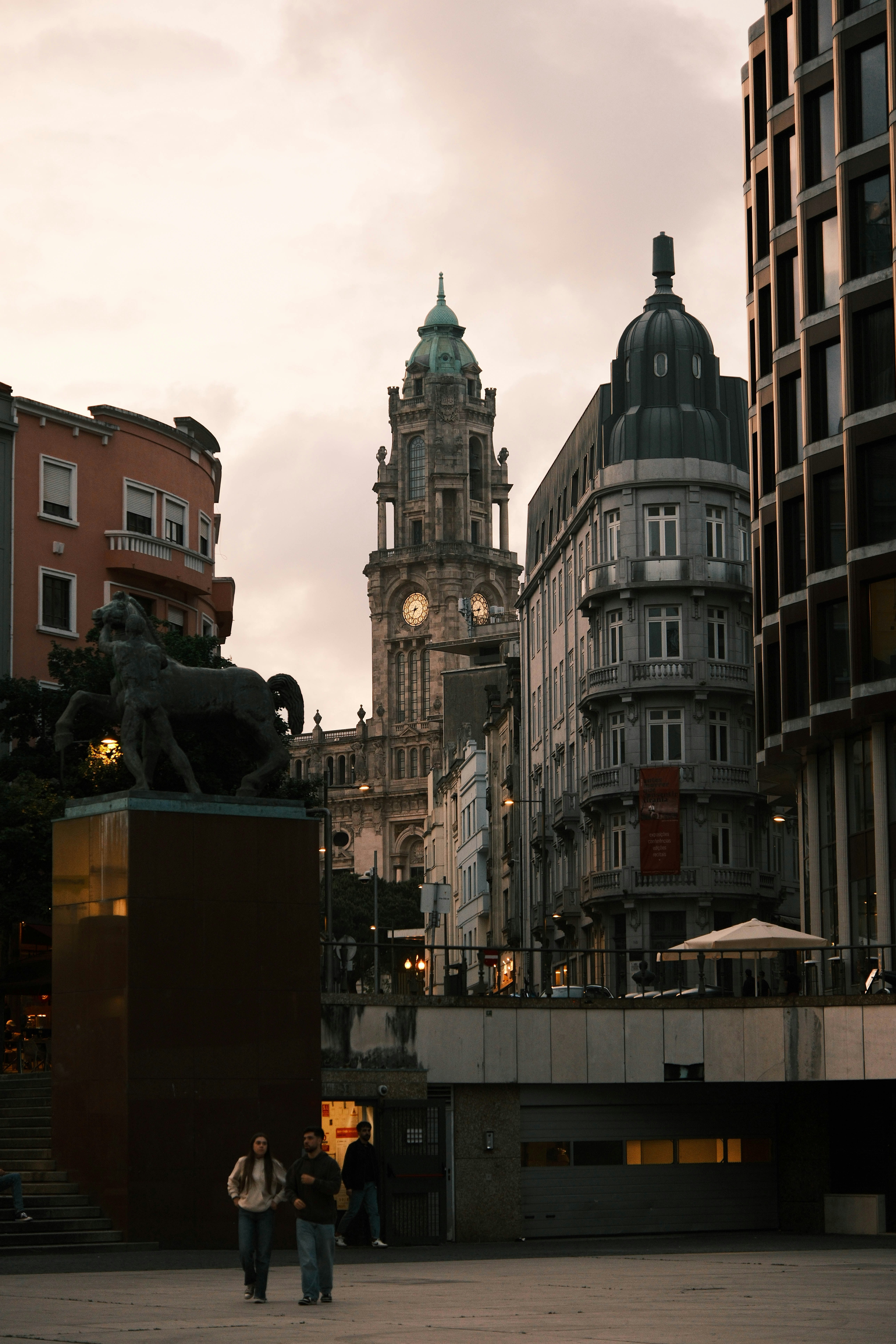 People walking in a city square with a clock tower and statue in Porto