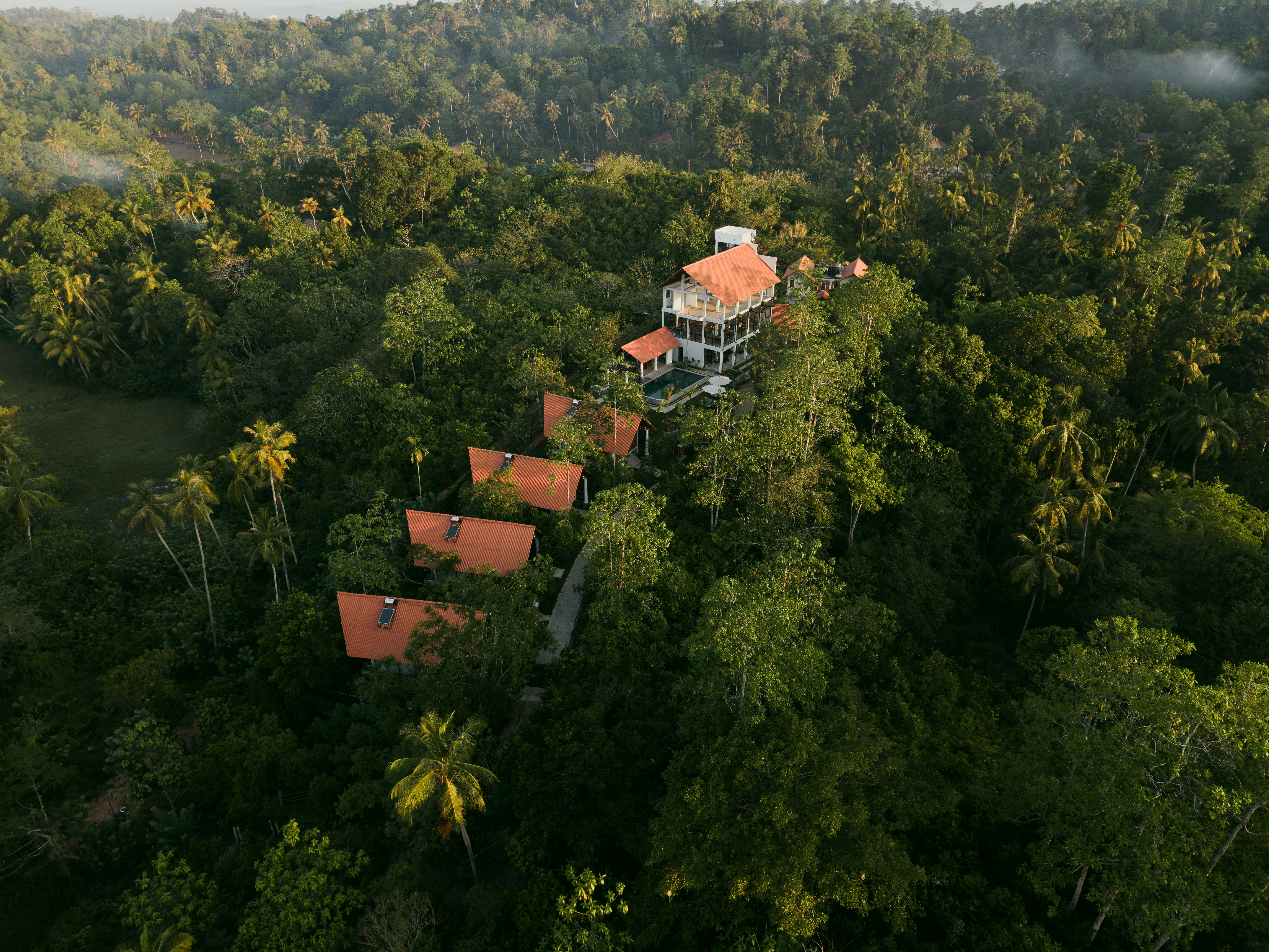 An aerial view of a resort with orange roofs nestled in a lush tropical forest