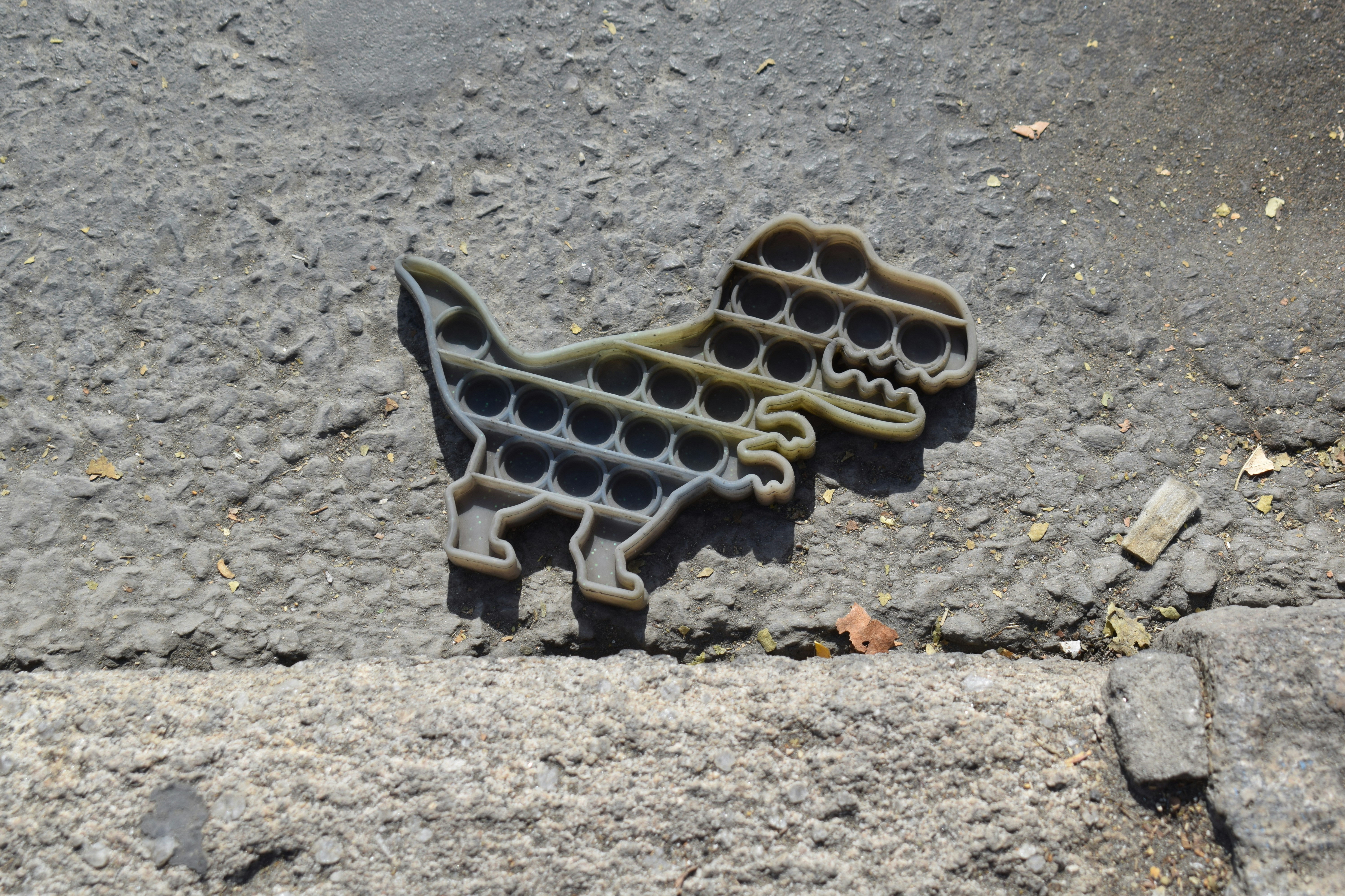 A grey dinosaur shaped silicone pop it toy on a rough asphalt surface