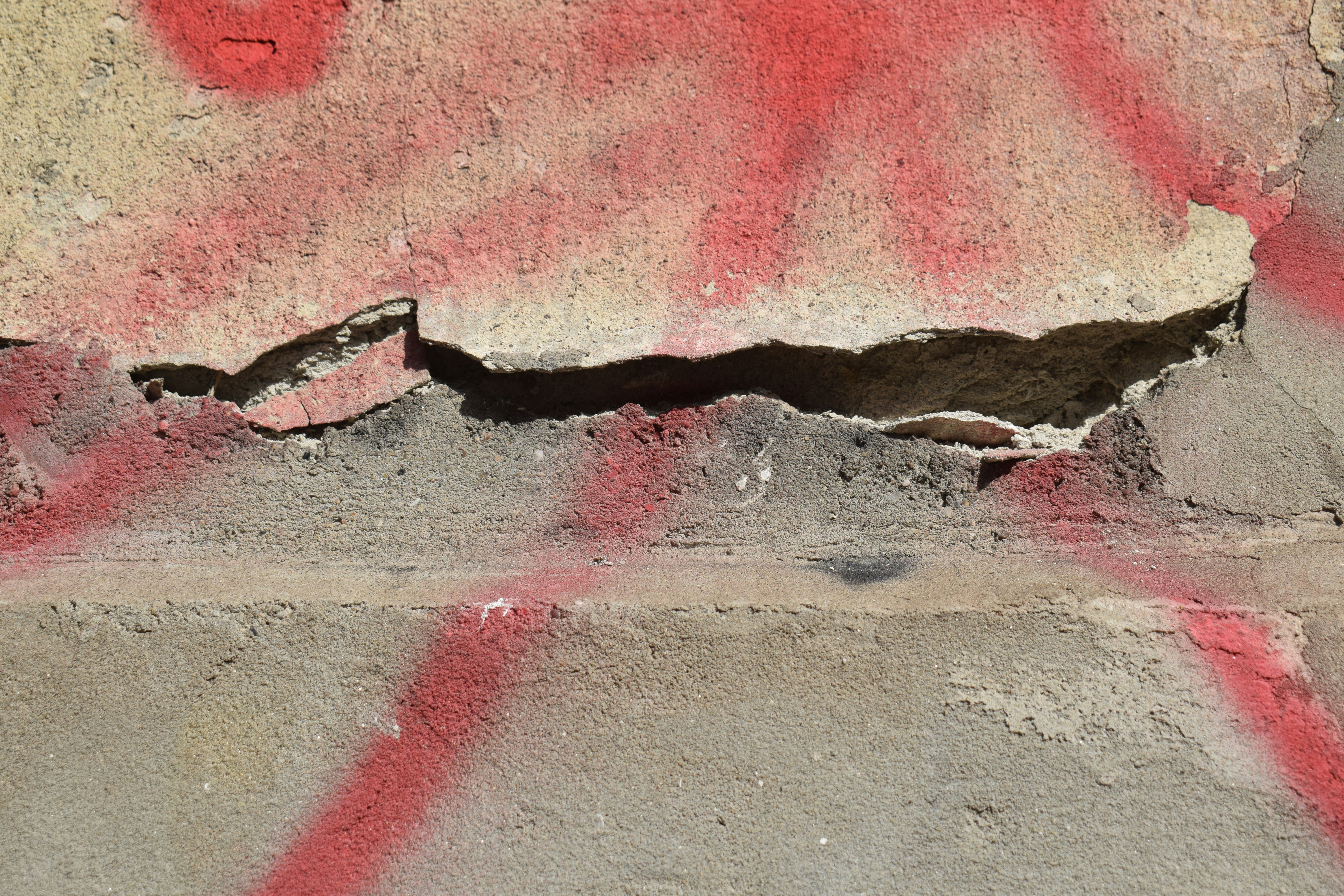 A cracked concrete wall with peeling plaster and faded red spray paint