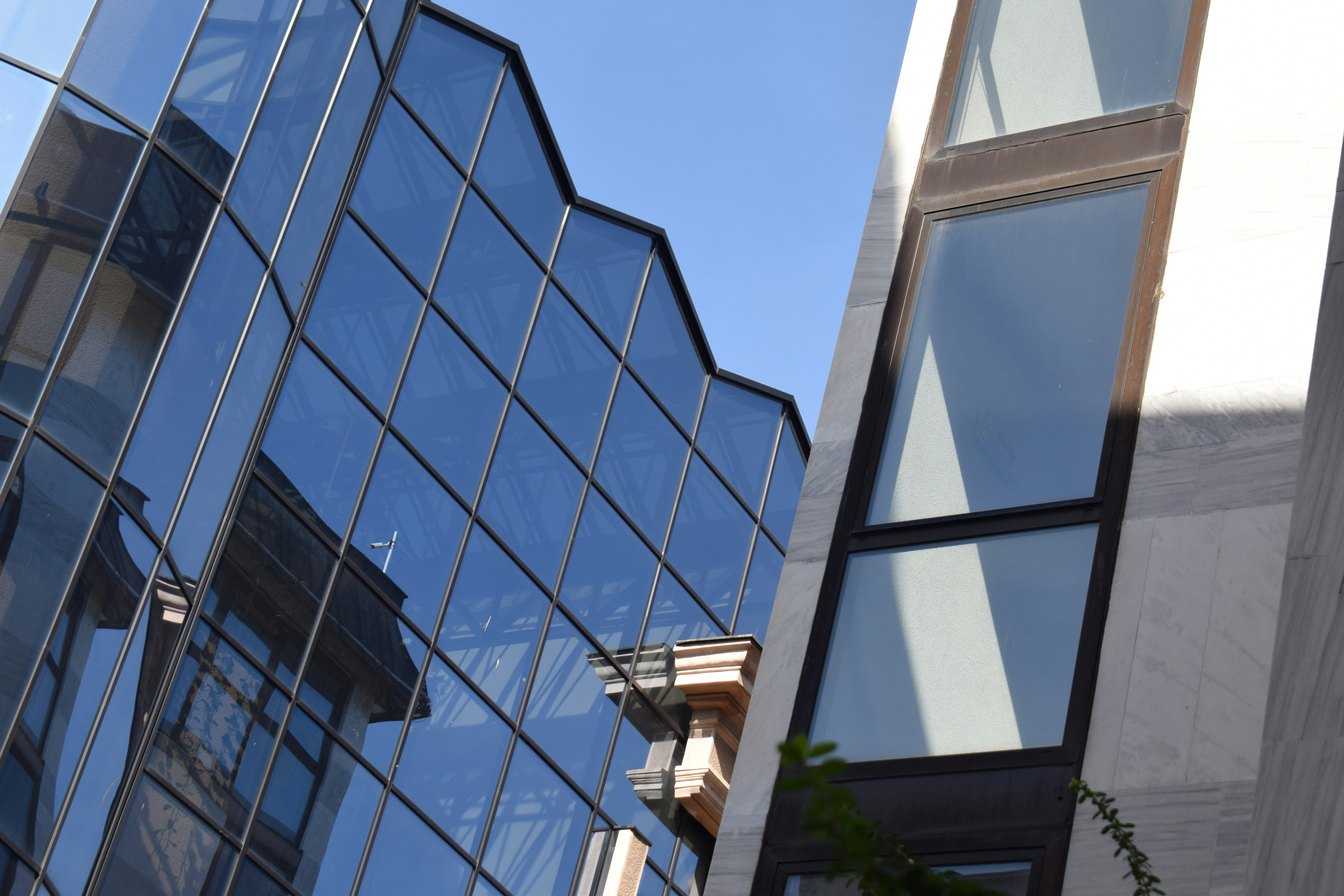 Modern glass office building facade reflecting a historic building against a clear blue sky