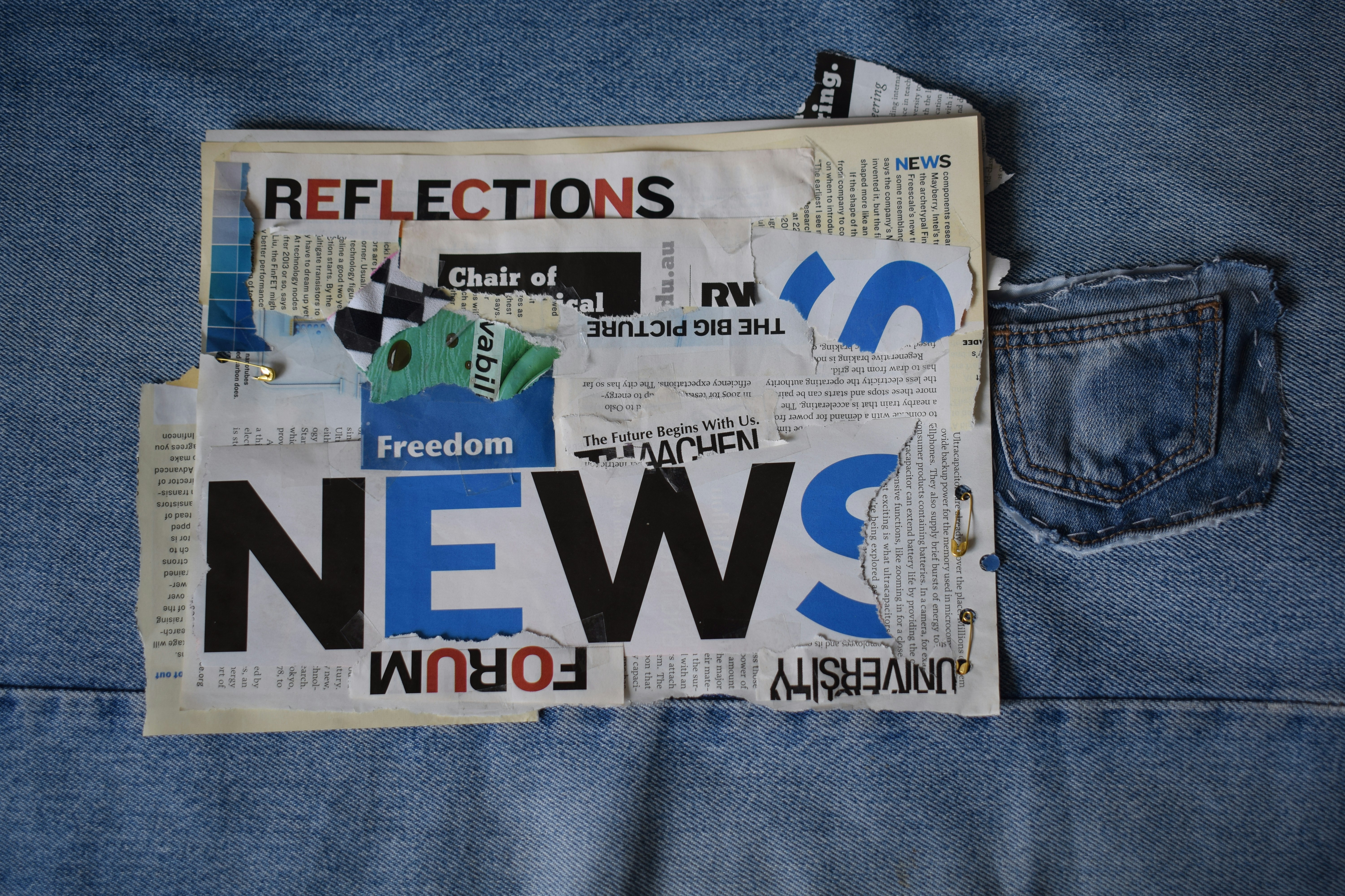 A collage of torn newspaper clippings and headlines pinned onto blue denim fabric