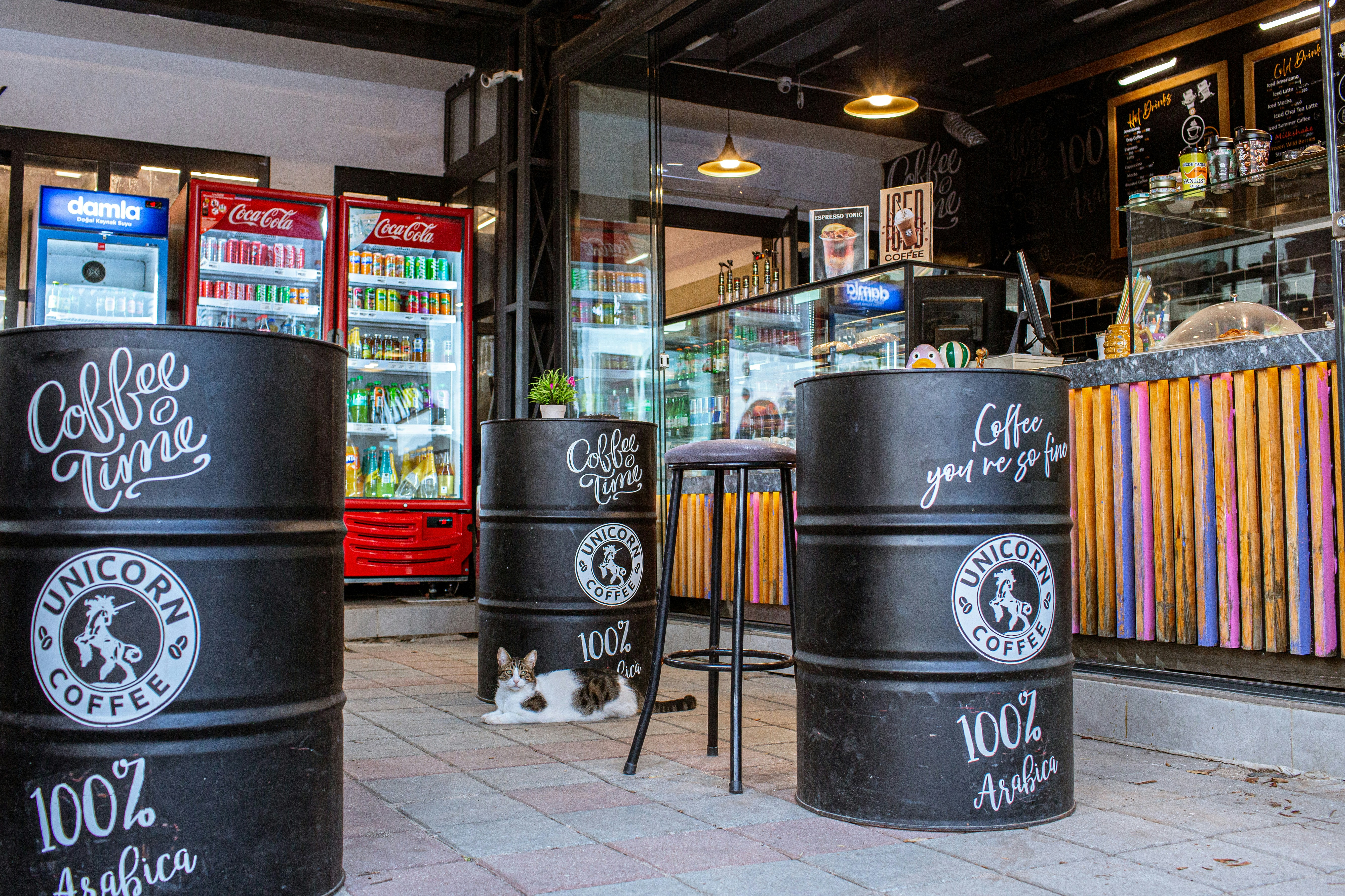 コーヒーショップの黒い樽のテーブルのそばのタイル張りのパティオで休んでいる猫