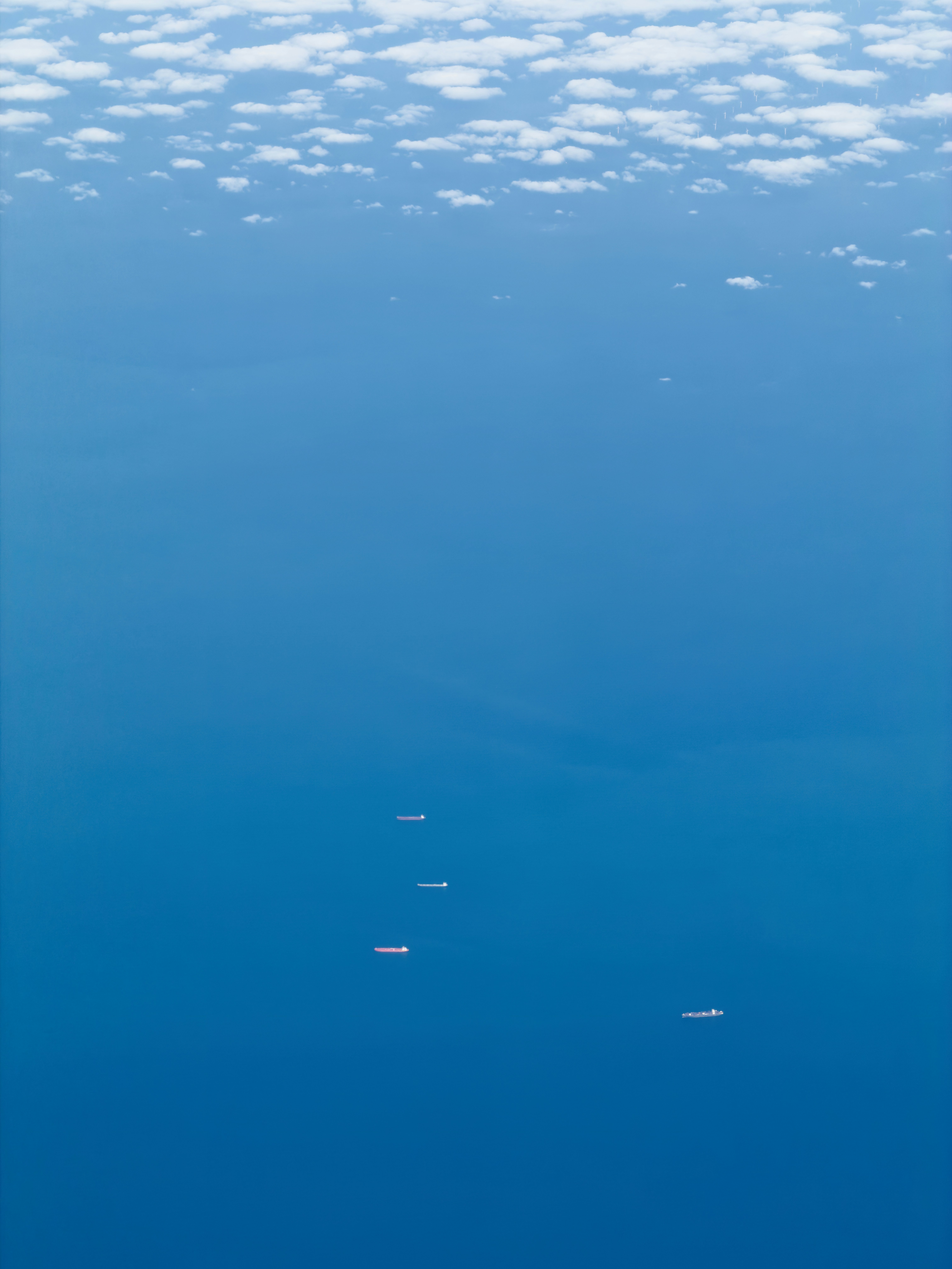 An aerial view of four cargo ships on the deep blue ocean under scattered clouds