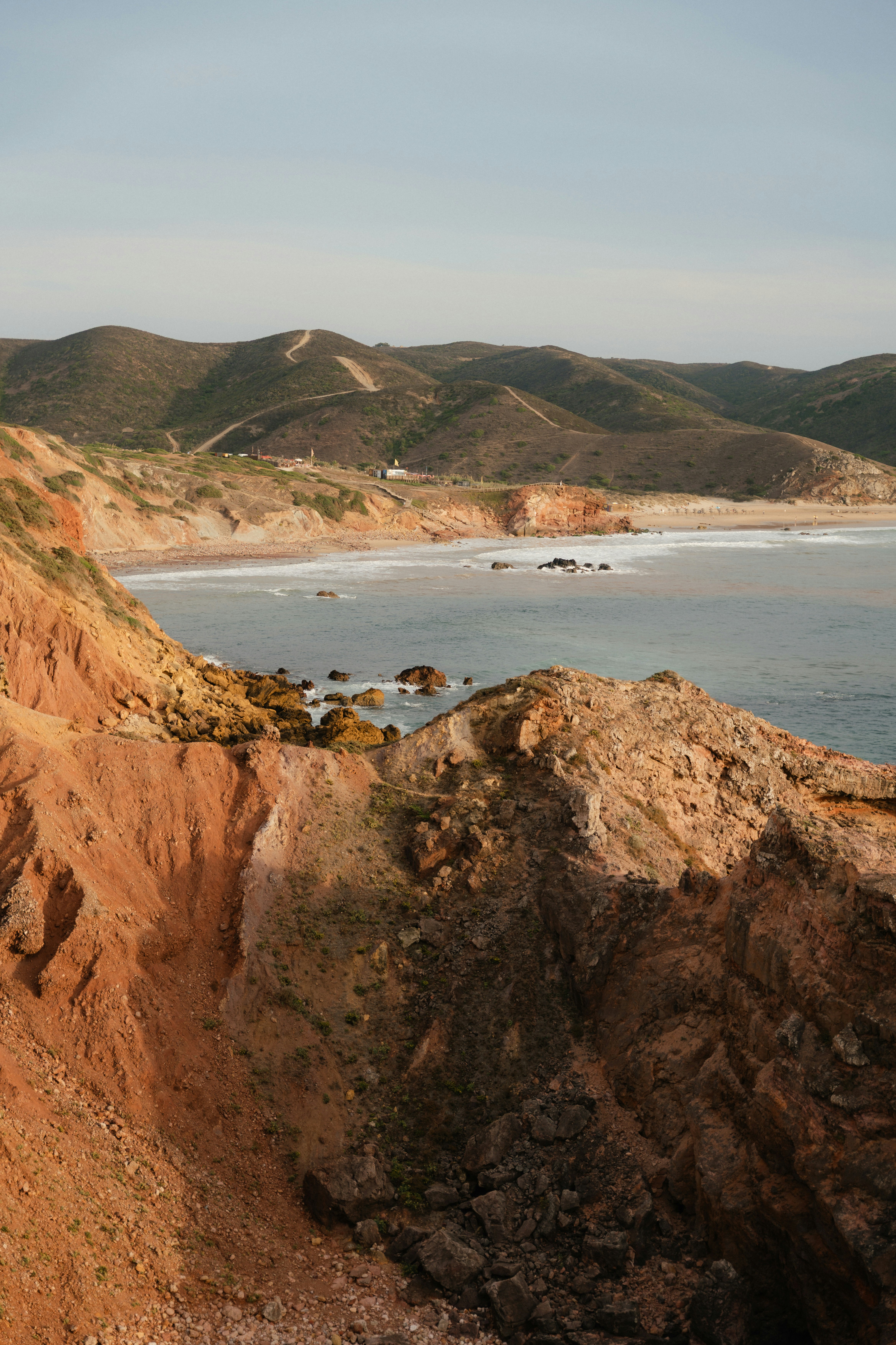 Rugged orange cliffs overlooking a sandy beach and the ocean under a clear sky