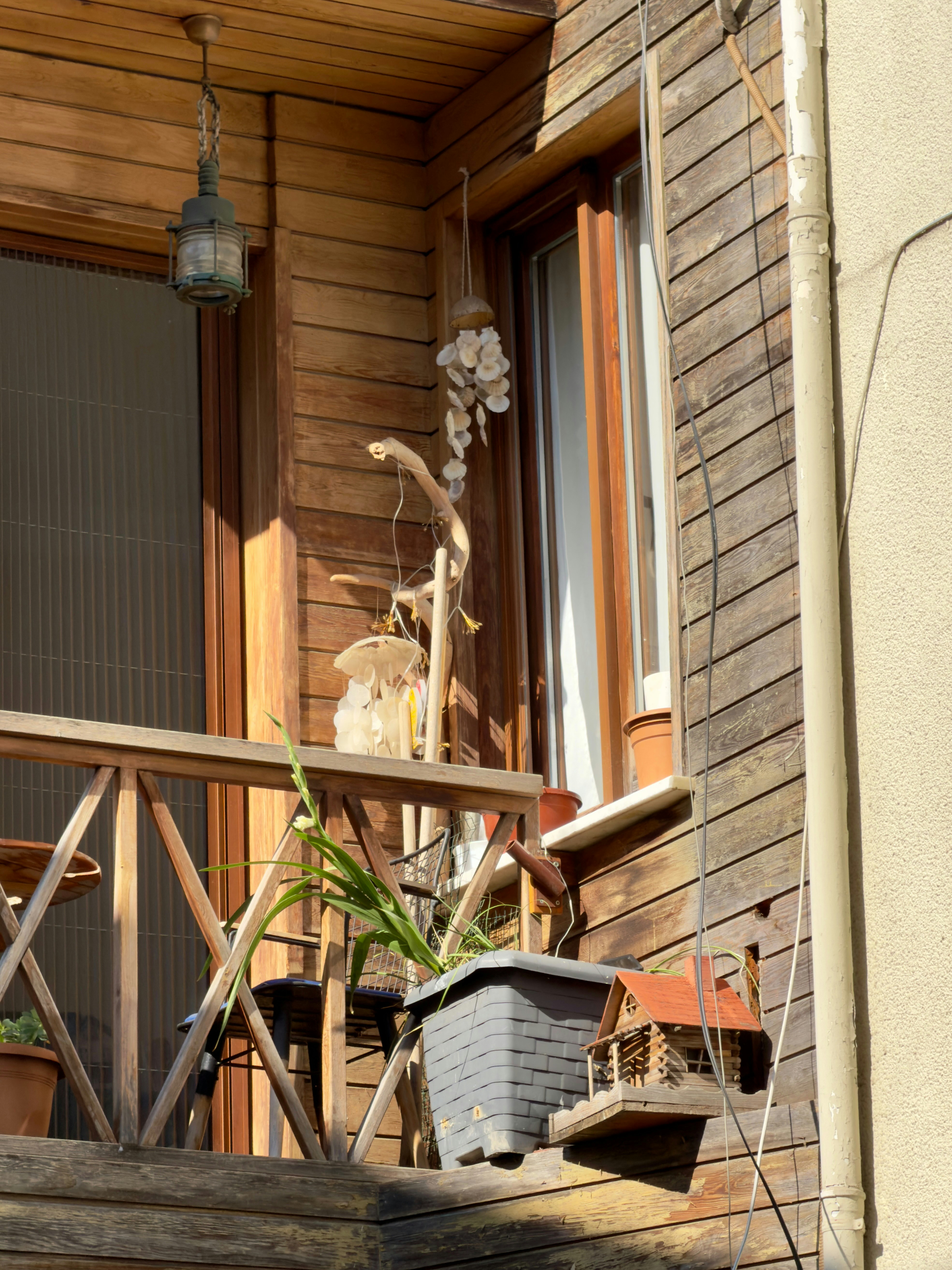 A wooden balcony with a shell wind chime, a potted plant, and a small birdhouse